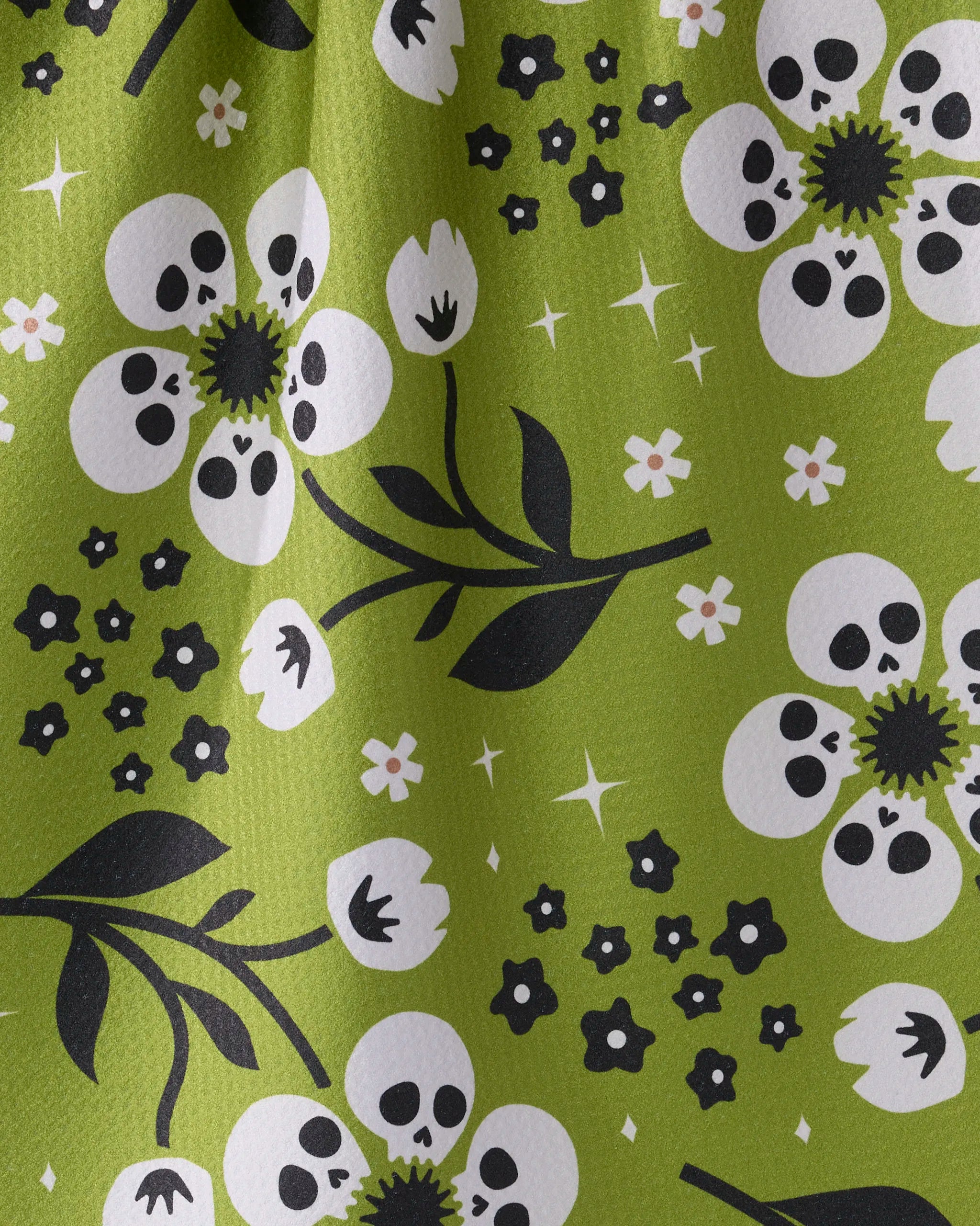 The Marrow Bloom tea towel by Geometry features a green floral pattern with white flowers, black skull-like centers, and starbursts—made from recycled materials for exceptional absorbency.