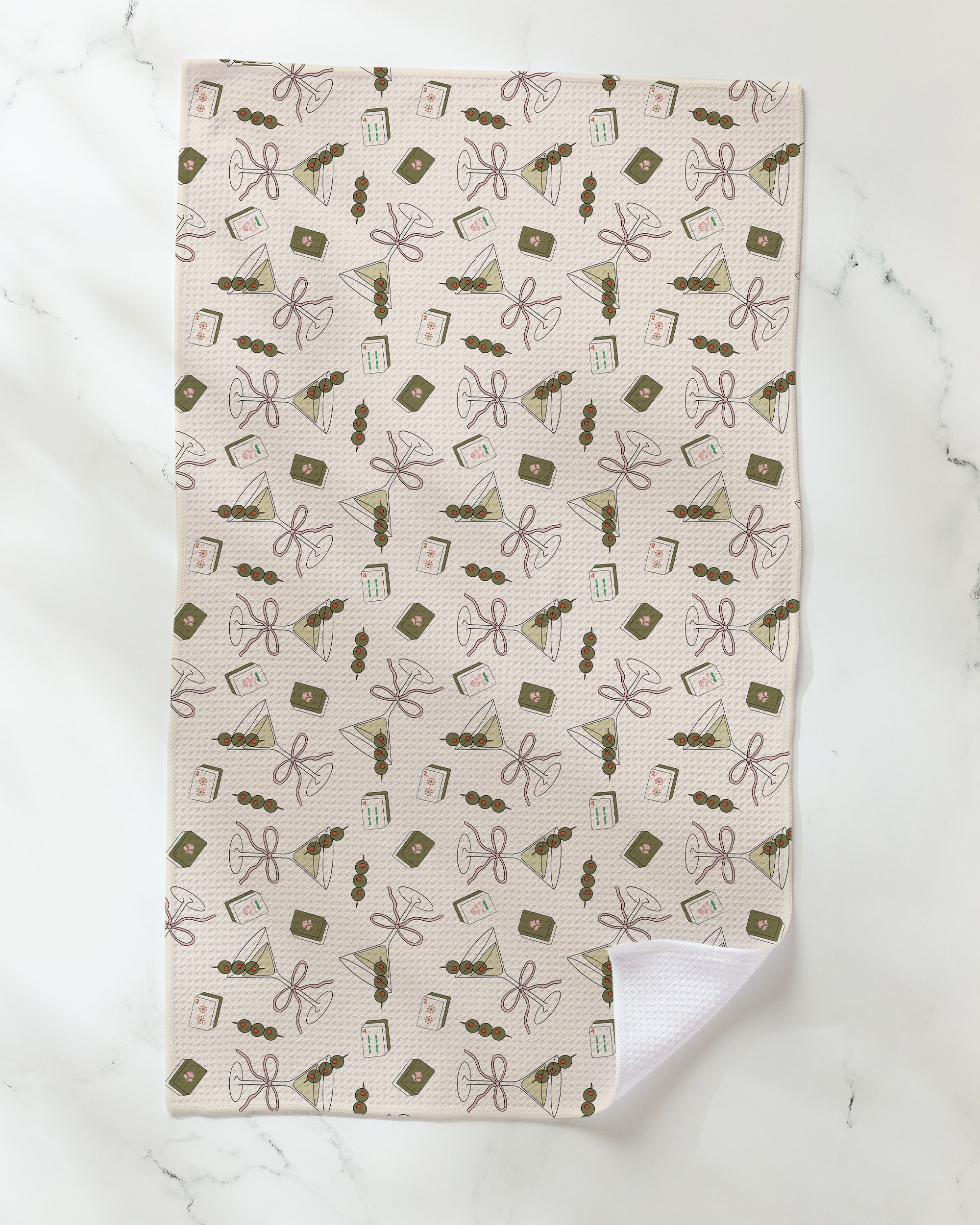Introducing the "Martini Tiles" towel by Geometry—a white, ultra-absorbent towel adorned with a delicate pastel pattern of bows, books, candles, and charming decorative objects. Resting elegantly on a marble surface, it’s the perfect eco-friendly kitchen or tea towel to add style and function to your home.