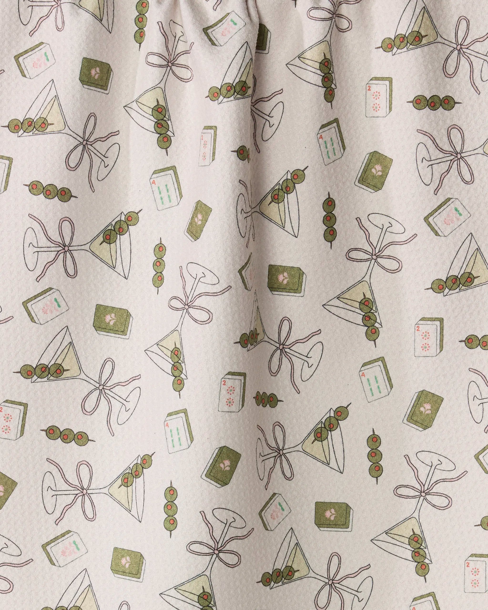 Martini Tiles by Geometry features a playful, patterned fabric showcasing martini glasses with olives, triangular sandwiches, and playing cards on a light background. The brown-outlined illustrations are accented in green and pink—ideal for use as a whimsical tea towel or kitchen towel made from recycled materials.