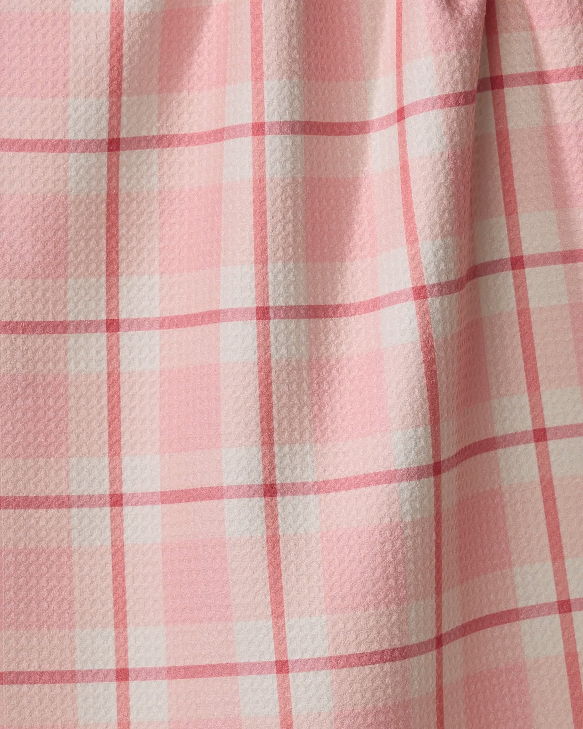 A close-up of the Marva Lu tea towel by Kelsi Fullmer shows pink Geoweave fabric with a white and dark pink plaid pattern, softly draped to display its textured surface and gentle folds.