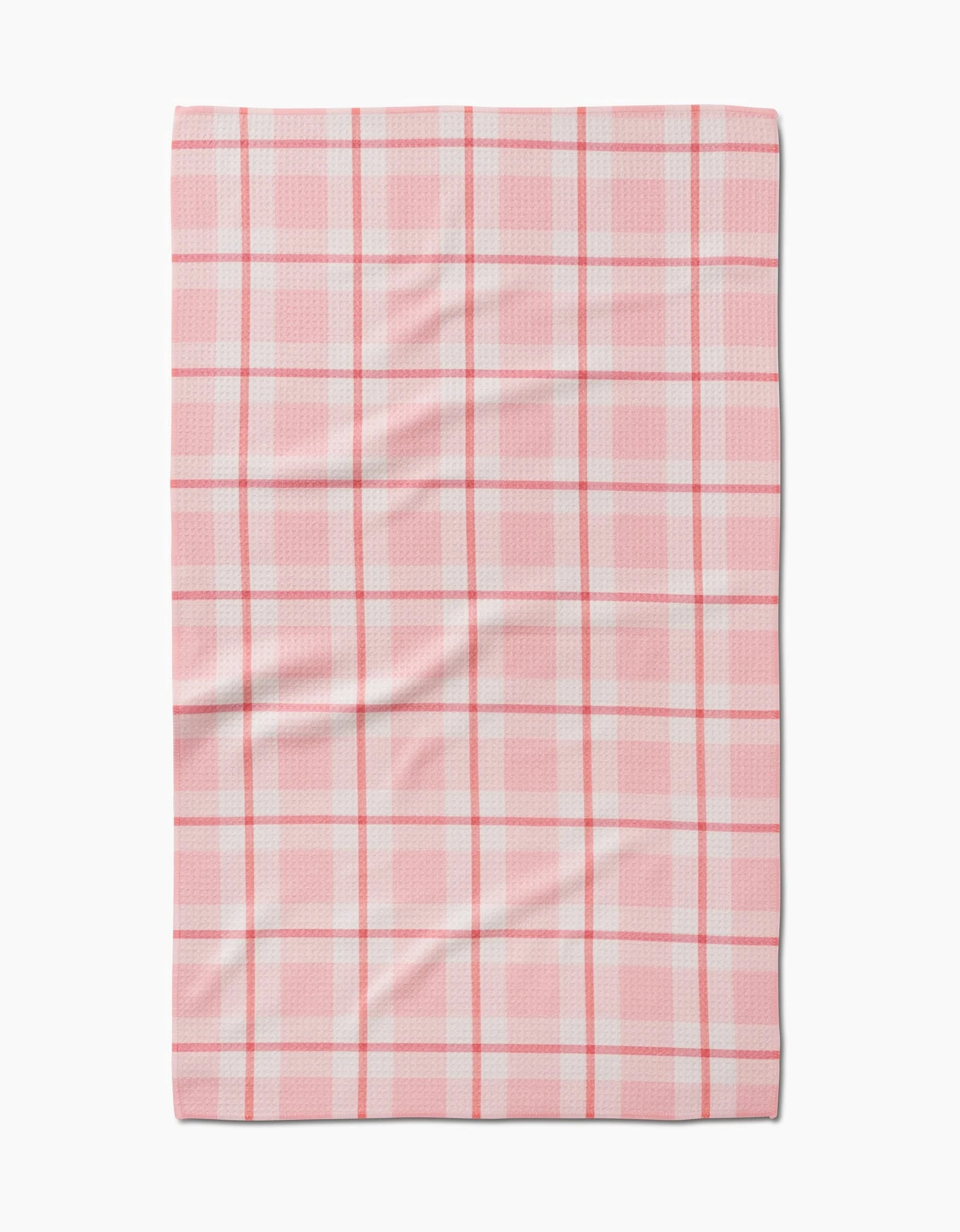 The Marva Lu tea towel by Kelsi Fullmer is rectangular, made from recycled materials, and showcases a pink and white plaid pattern with intersecting lines and gentle surface wrinkles.