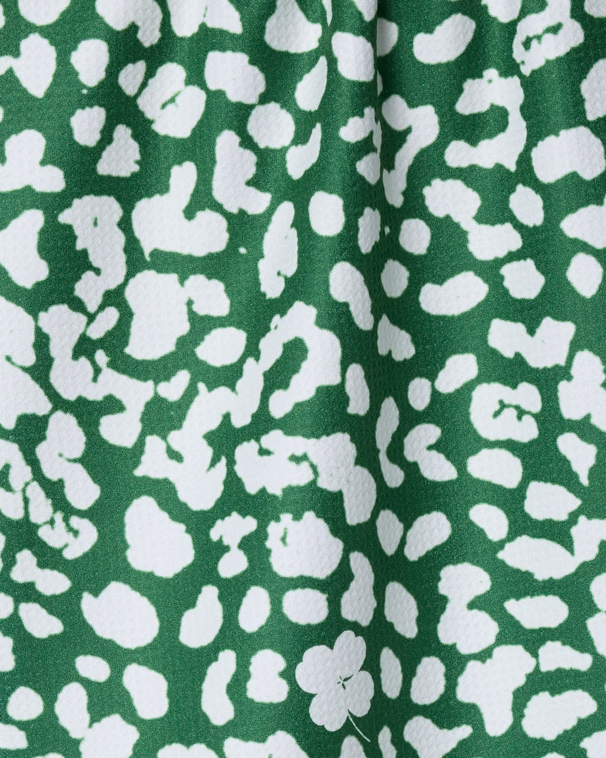 The Mas Feroz dish towel by Geometry features a green fabric with an abstract white leopard print, a slightly textured, absorbent surface, and irregular white spots across the background.