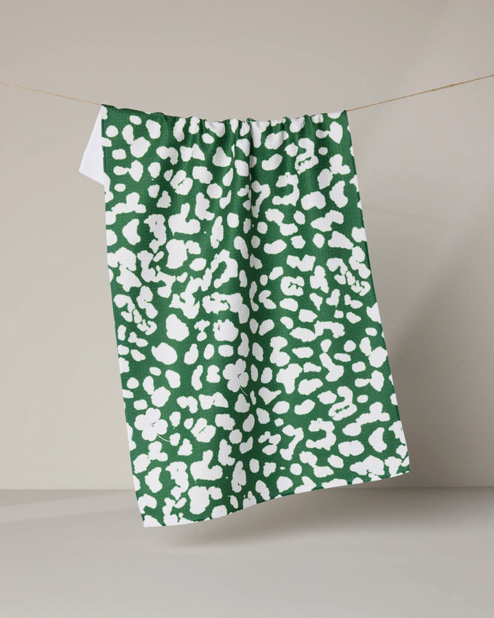 The Mas Feroz tea towel by Geometry, featuring an ultra-absorbent fabric and an abstract white spotted pattern, is shown hanging on a string against a neutral beige background.