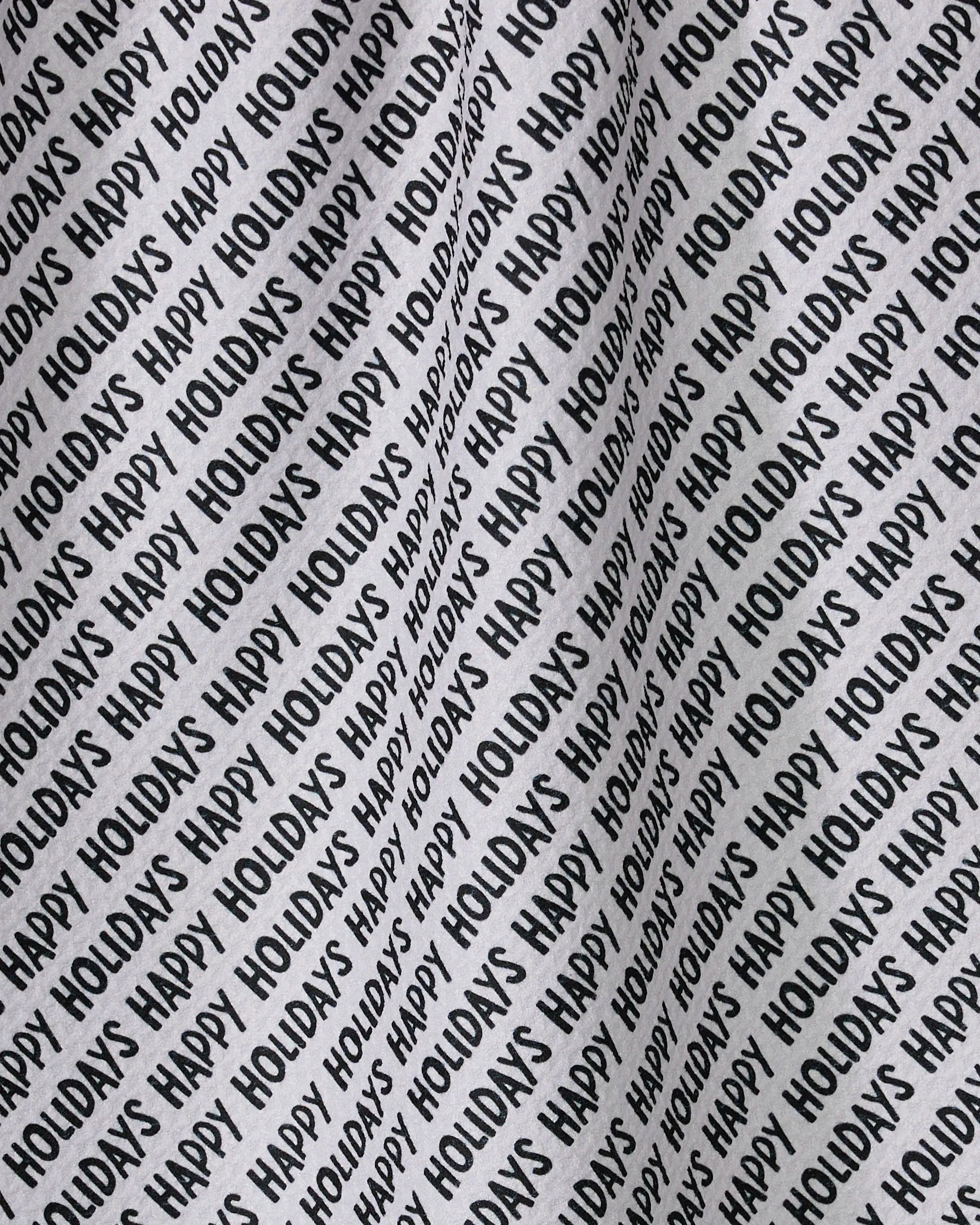 The Geometry Merrier tea towel features black "HAPPY HOLIDAYS" text in repeating diagonal lines across a white background, creating a festive, quick-drying holiday pattern.