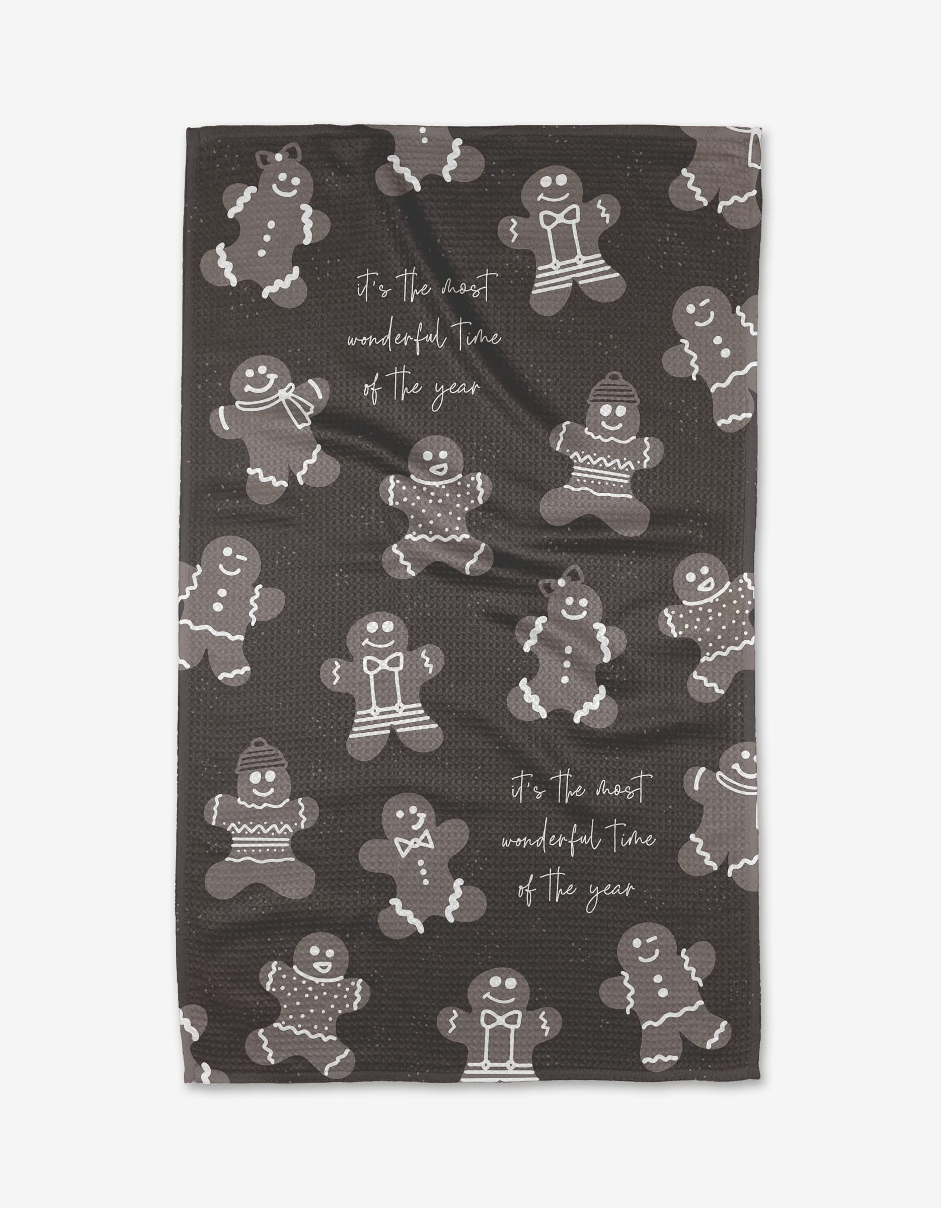 The Rosa Kichline Merry Gingerbread kitchen towel features black fabric with white and gray gingerbread people and the phrase “it’s the most wonderful time of the year,” making it a festive, eco-friendly tea towel made from recycled materials.