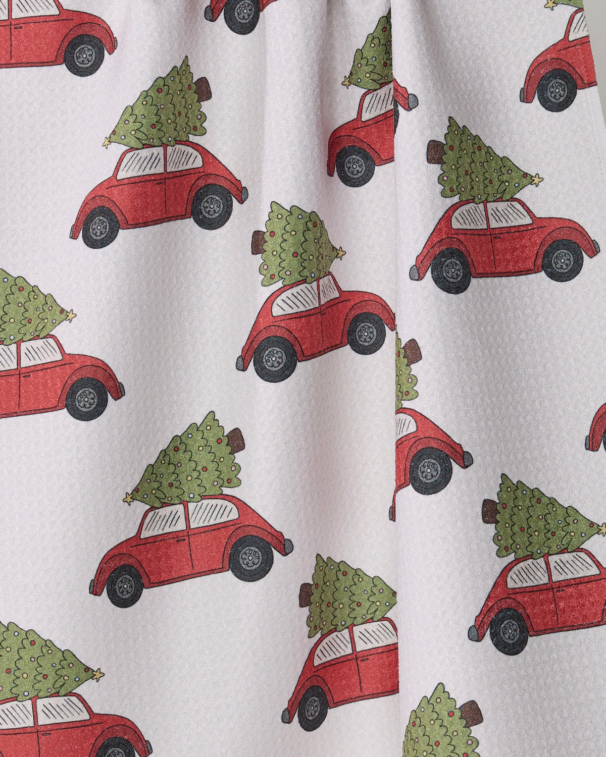 Introducing “Merry Miles” by Geometry—a patterned fabric featuring playful, cartoon-style red cars carrying Christmas trees atop, repeated across a crisp white background. This festive design is perfect for an eco-friendly tea towel made from recycled materials.
