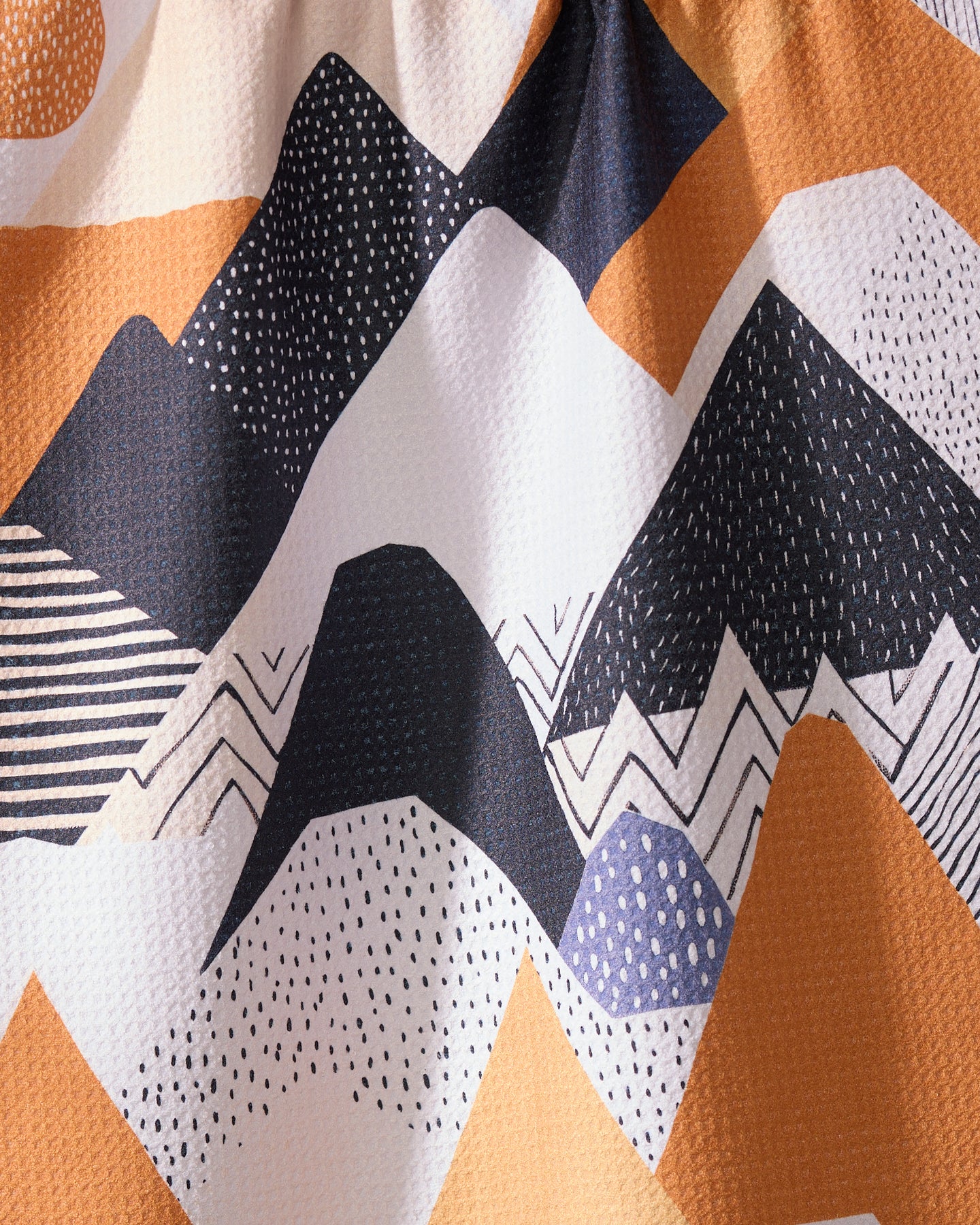 Mesa Rise by Geometry features an abstract illustration of overlapping mountains in black, white, and orange with dotted, lined, and zigzag patterns on a textured tea towel made from recycled materials.