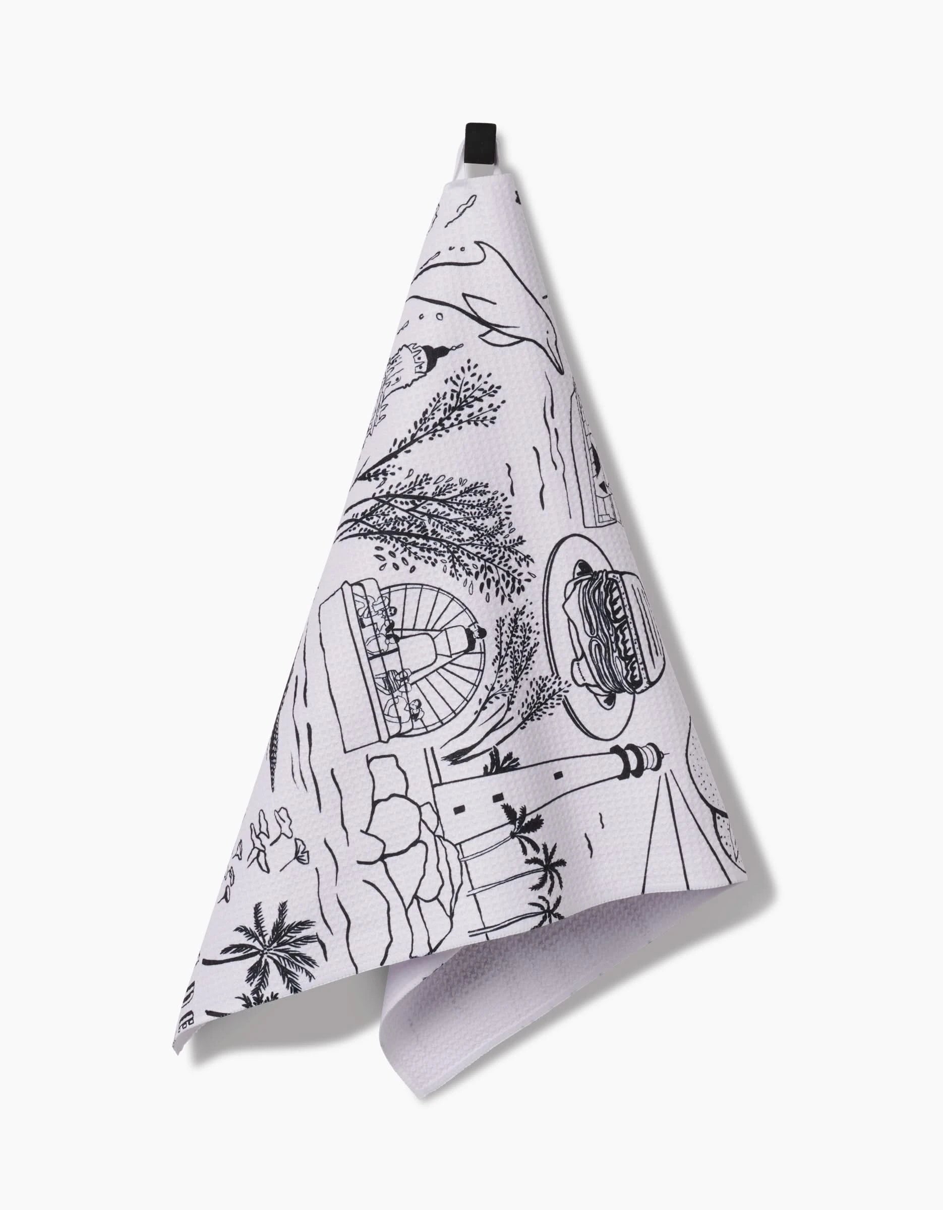 The Elisabeth Wing “Miami” Tea Towel features black beach scene line art—palm trees, lighthouse, ocean waves, burger, window—on white Geoweave™ fabric with a black hanging loop.