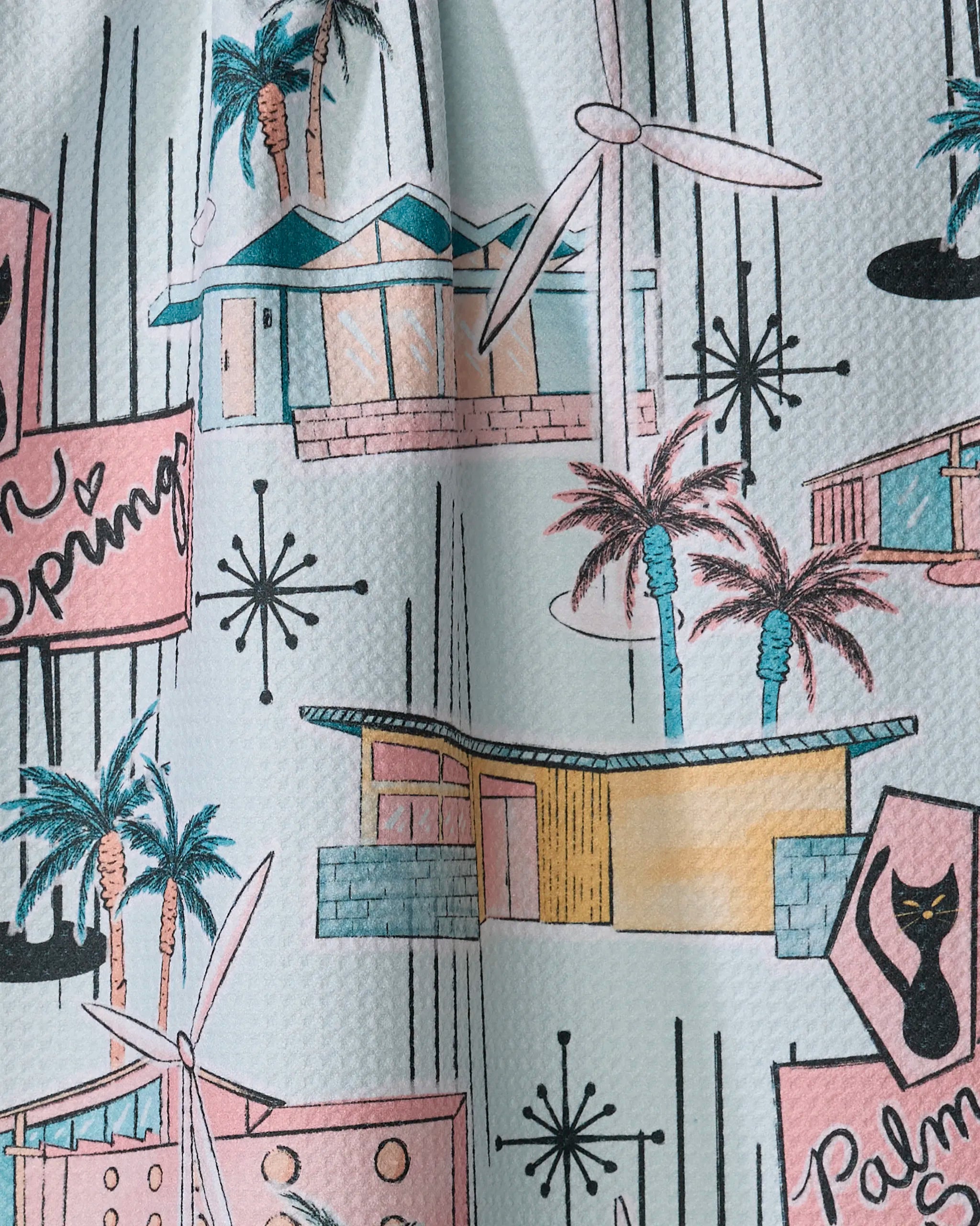 Julianne Haness’s ‘Mid Century’ tea towel showcases vibrant houses, palm trees, wind turbines, and atomic starbursts for a vintage Palm Springs vibe—perfect in your kitchen and quick-drying.