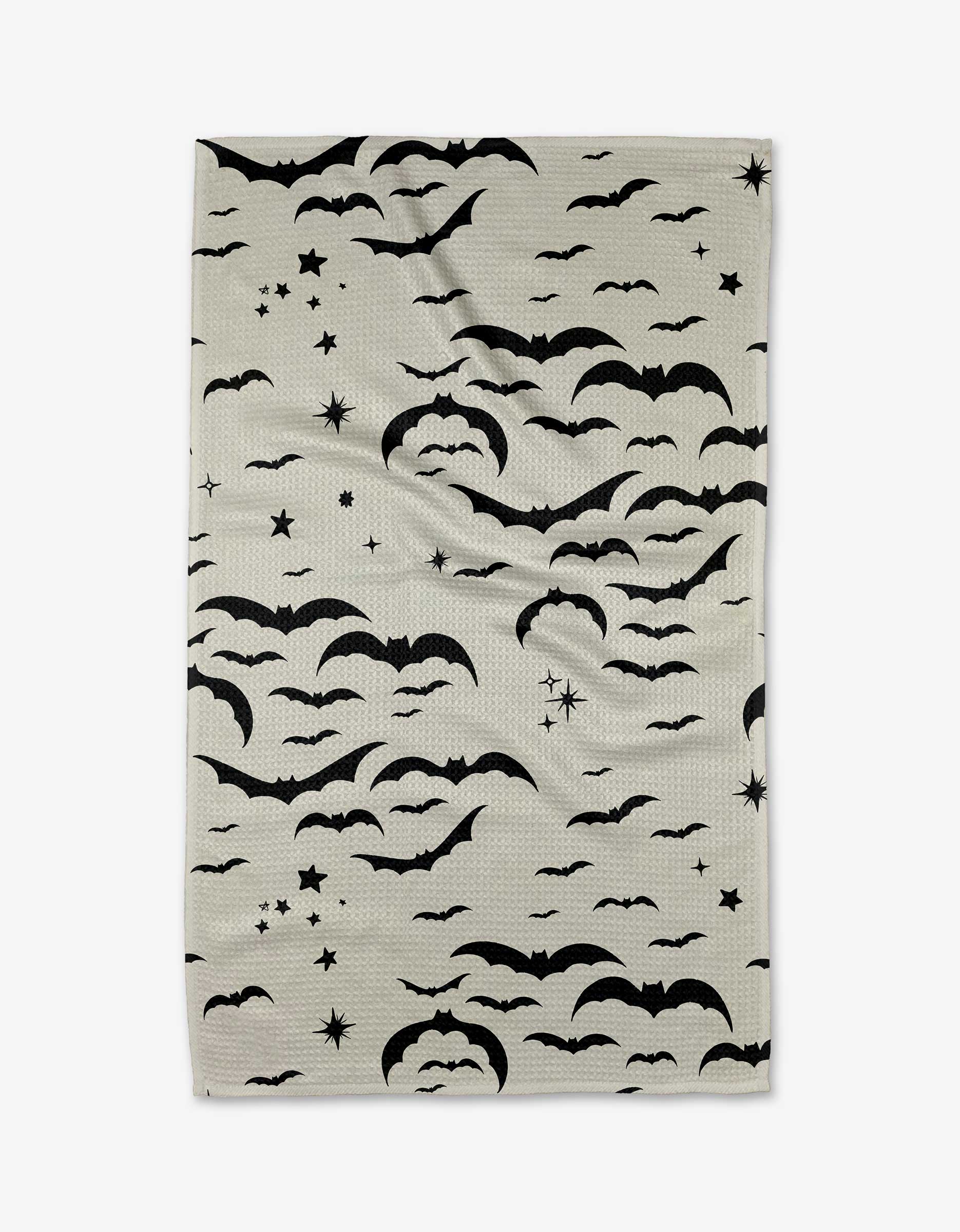 The Midnight Bats kitchen towel by Danelys Sidron is a light beige, recycled, ultra-absorbent towel featuring black bats, clouds, stars, and crescent moons in its pattern. It appears slightly wrinkled against a white background.