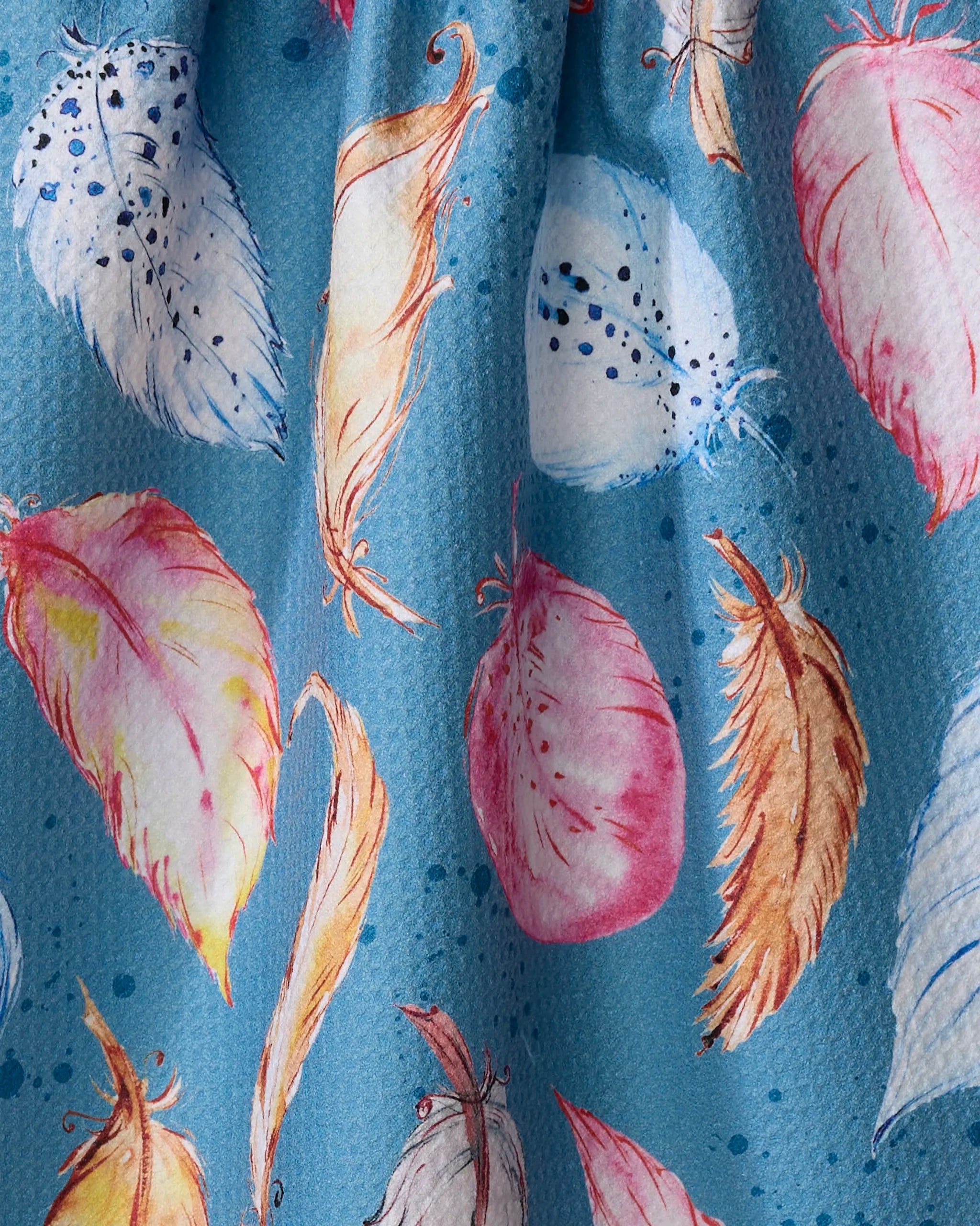 A close-up of Elena Fay's "Midnight Breeze" tea towel, featuring blue fabric adorned with colorful watercolor-style feathers in pink, white, orange, and brown, accented by scattered blue dots.