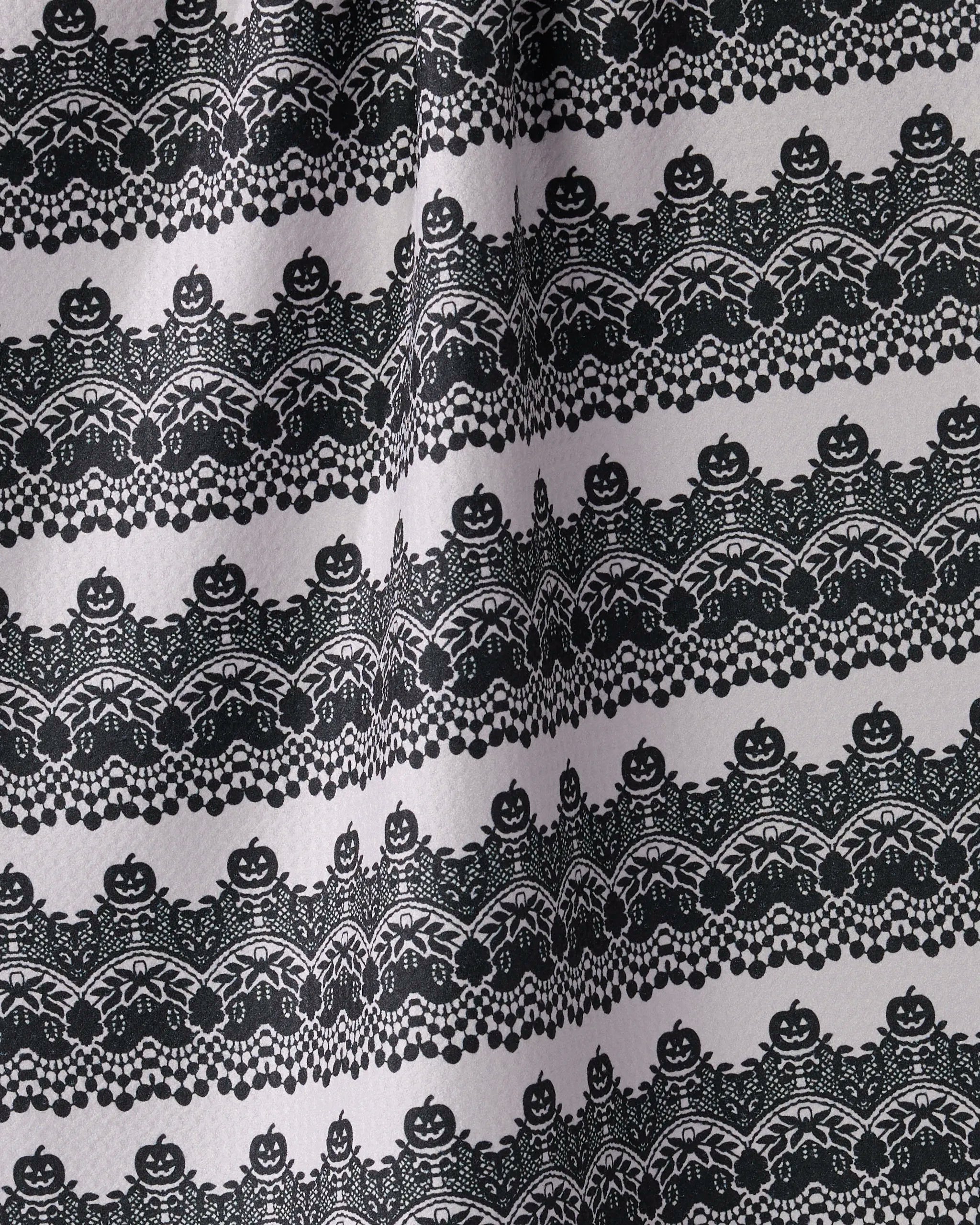 The Geometry Midnight Lace tea towel features black and white horizontal rows of jack-o-lanterns, bats, spiderwebs, and lace-like patterns. Made from recycled materials for a festive, ultra-absorbent Halloween look.