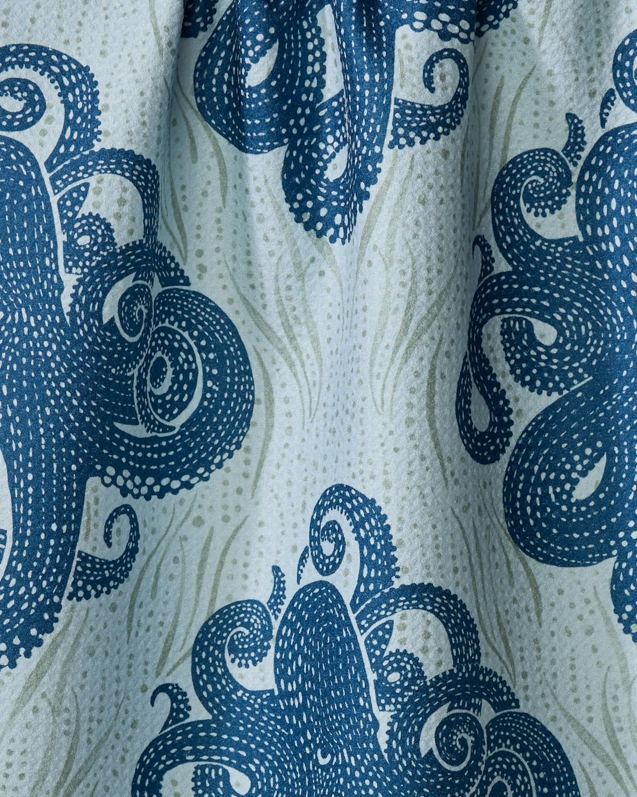 The Mighty Octopus tea towel by Katie O'Shea features blue octopus illustrations with white dot patterns on a wavy light blue background, creating a marine-inspired, ultra-absorbent, and textured fabric look.