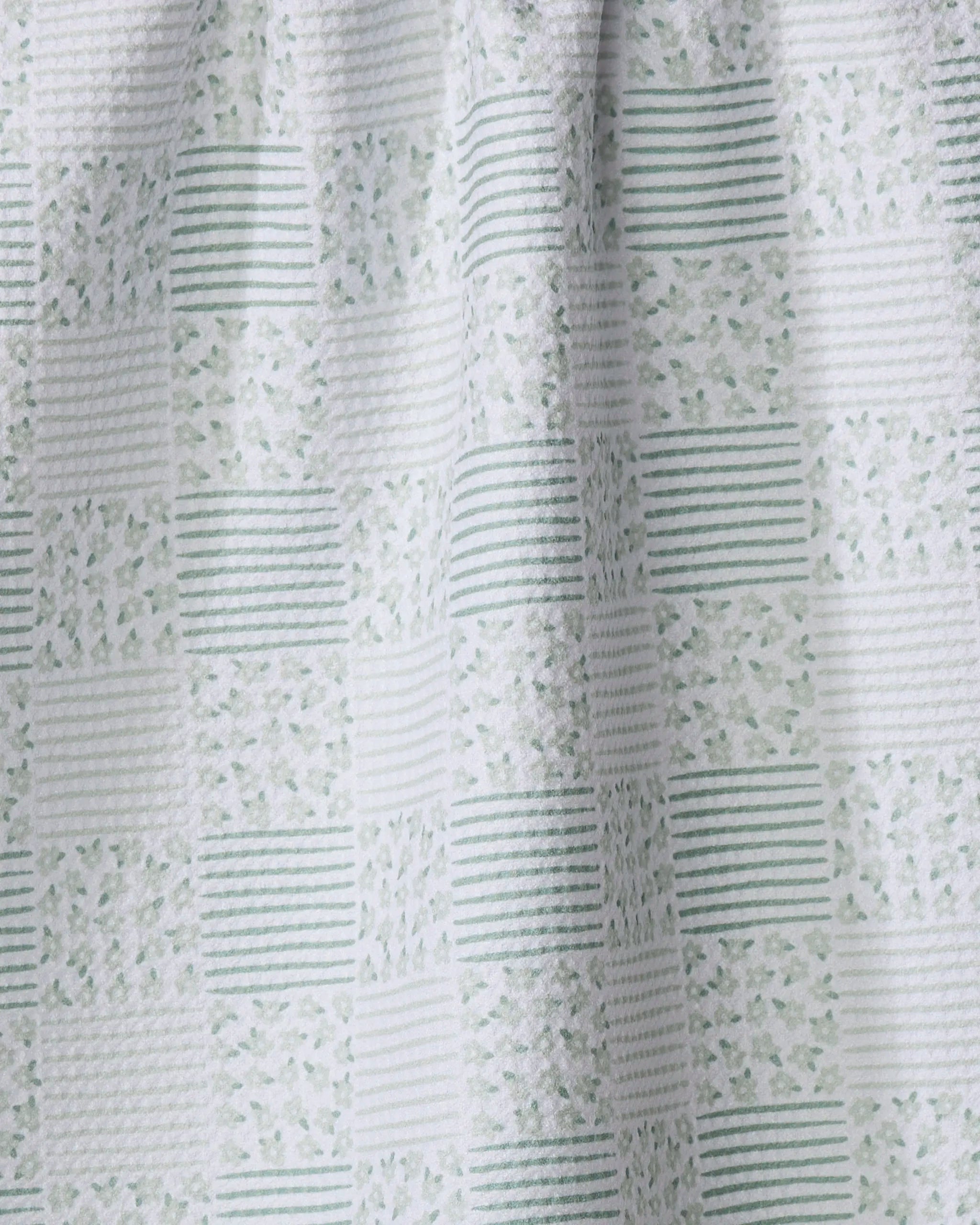 A close-up of Hufton Studio's Mini Flowers and Stripes Check Green tea towel fabric, showcasing a quick-drying textured checkerboard pattern with alternating green stripes and small floral motifs on a white background.