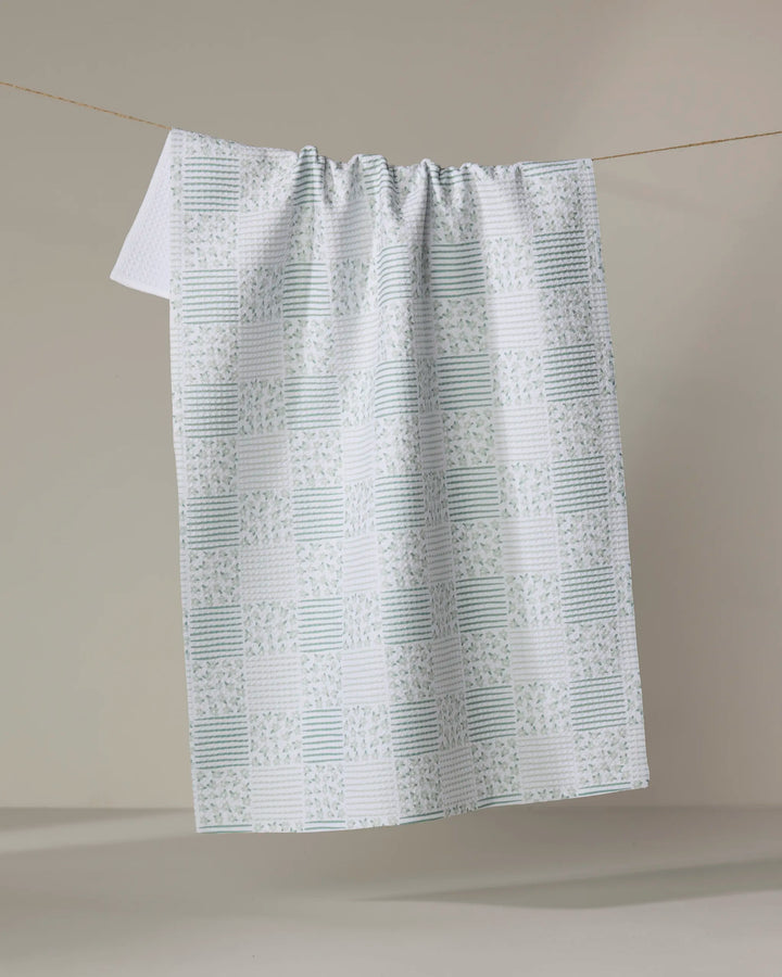 A quick-drying green checkered tea towel, the Hufton Studio Mini Flowers and Stripes Check Green, features alternating squares of stripes and floral patterns, draped over a clothesline against a neutral background.