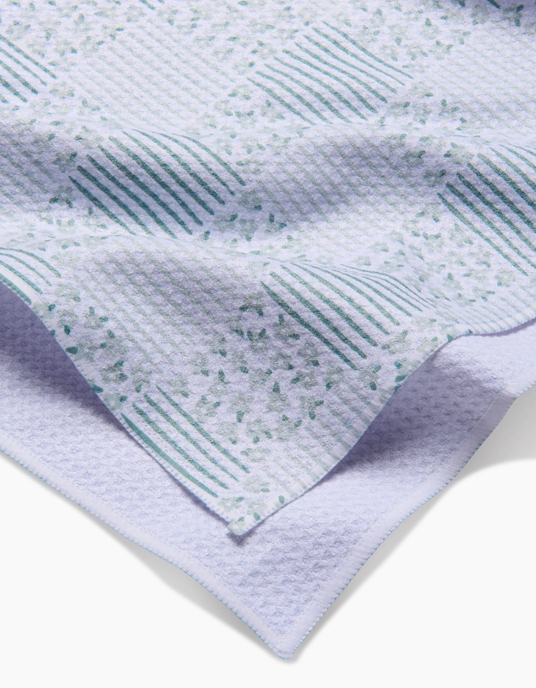 A close-up of Hufton Studios Mini Flowers and Stripes Check Green tea towel, folded to show its white waffle texture and teal-green checkered floral design, with the towel’s edge displayed against a white background.