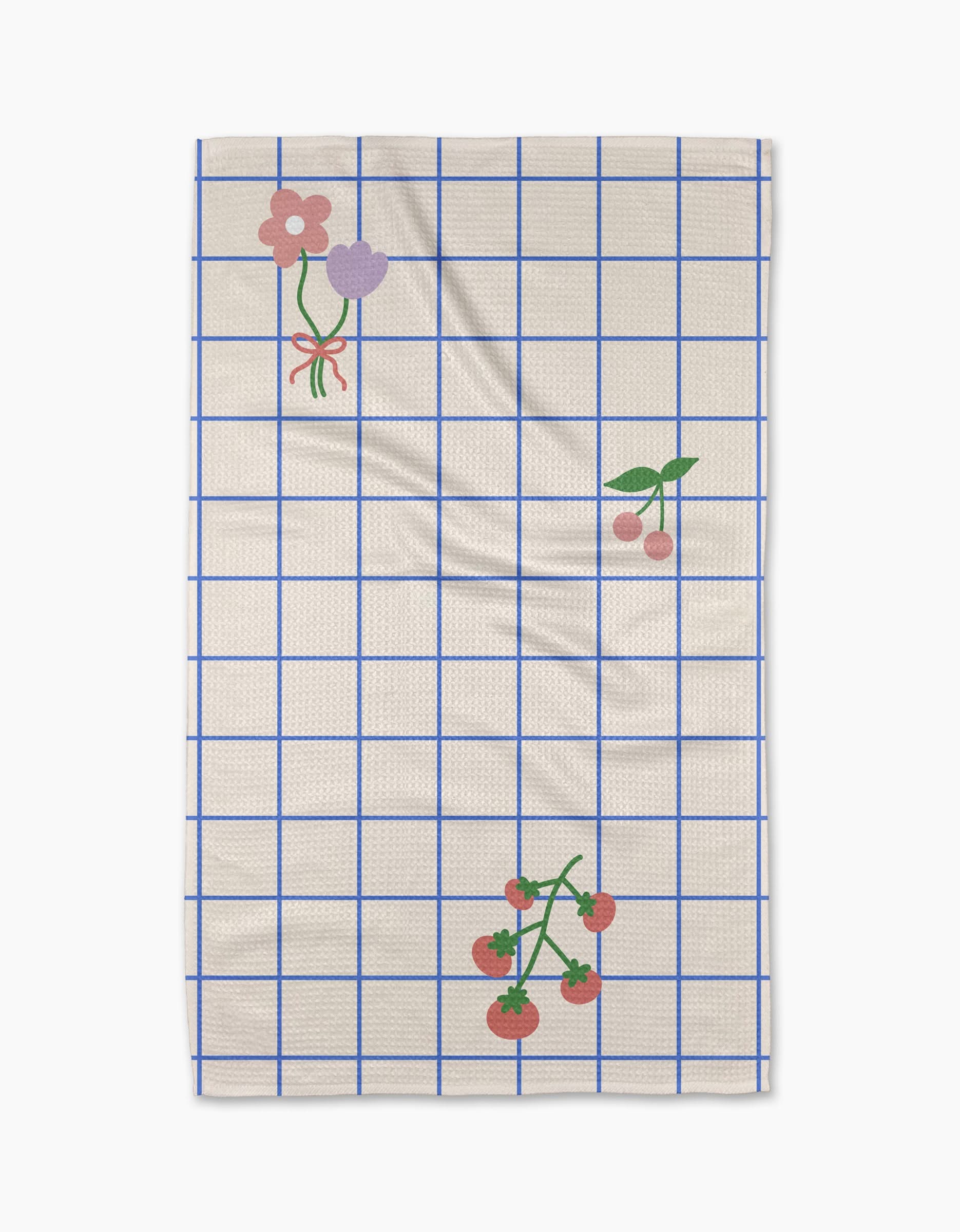 The Mini Harvest tea towel by Letters By Shells features a cream base with a blue grid, decorated with pink and purple flowers, cherries, and tomatoes—crafted from recycled materials for an eco-friendly touch.
