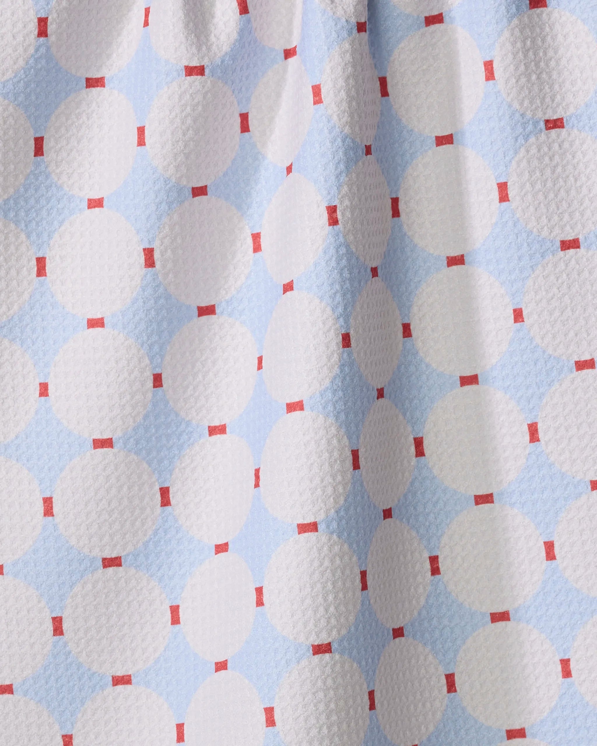 The Mist Blue Oasis tea towel by Happy Hemera is made from recycled materials, with large white circles on a light blue background bordered by red squares, and features a slightly textured, waffle-like surface.