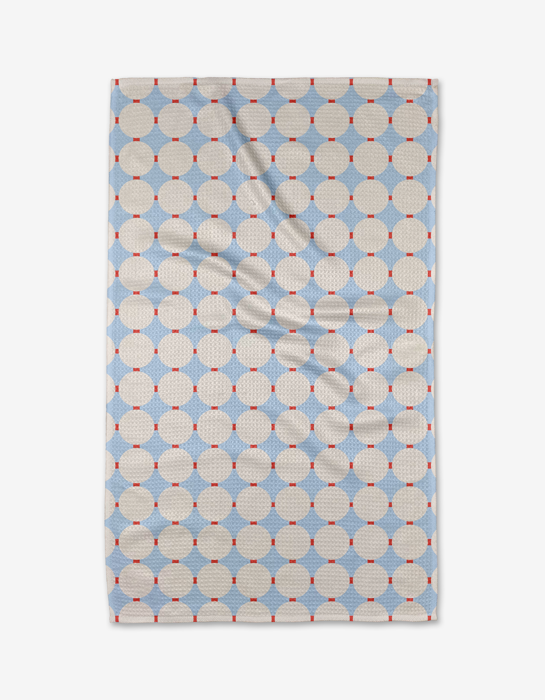 The Mist Blue Oasis tea towel by Happy Hemera features a geometric pattern of cream circles, blue diamonds, and red dots on a light background. Made from recycled materials, the fabric has some visible creases.