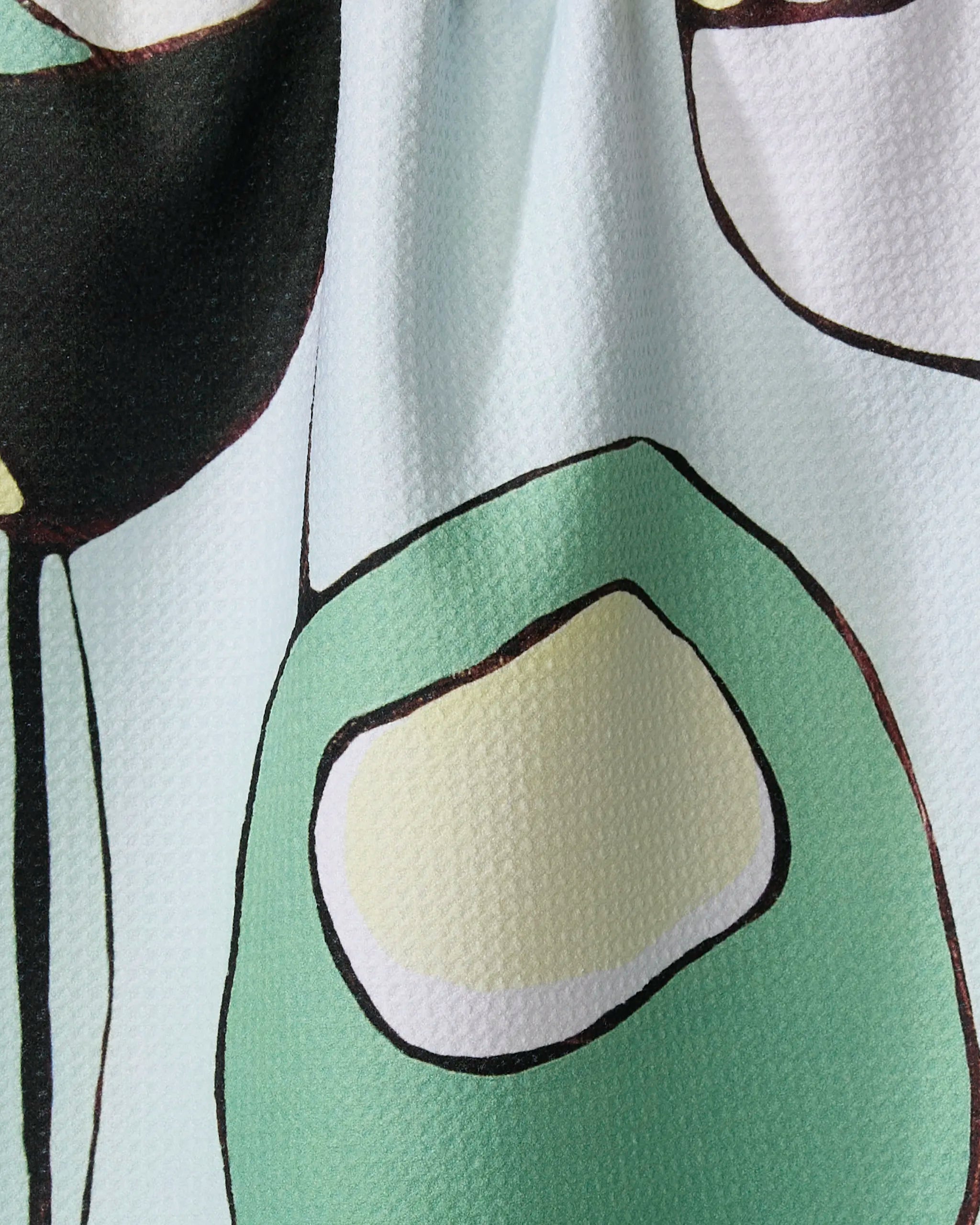 Close-up of Rachel Austin's "Modern Poppy" recycled kitchen towel, featuring an abstract pattern with black, white, light green, and yellow shapes outlined in black on a textured light background.