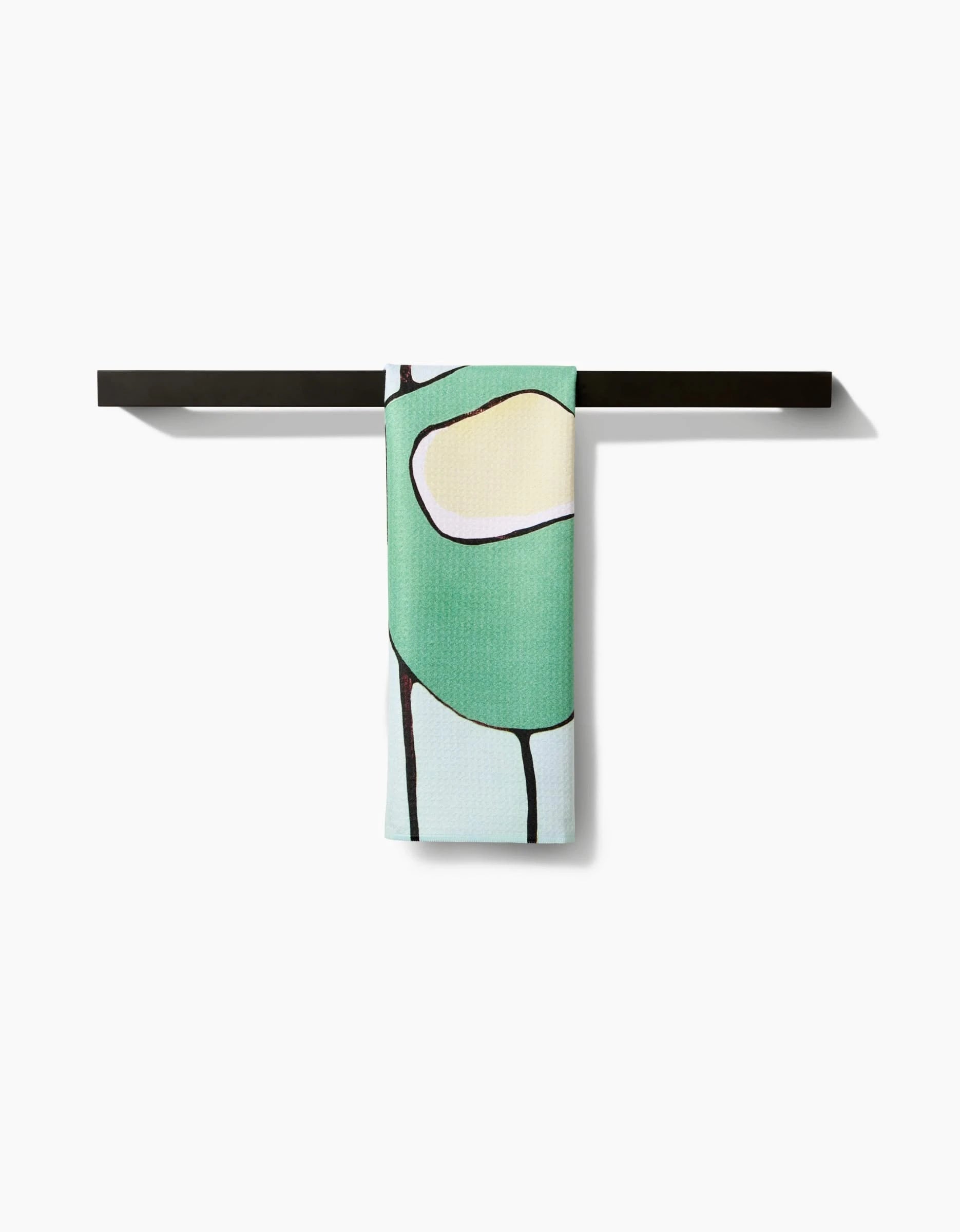 A vibrant Rachel Austin Modern Poppy tea towel with an abstract design in green, yellow, and black hangs neatly from a black horizontal rack against a white background.