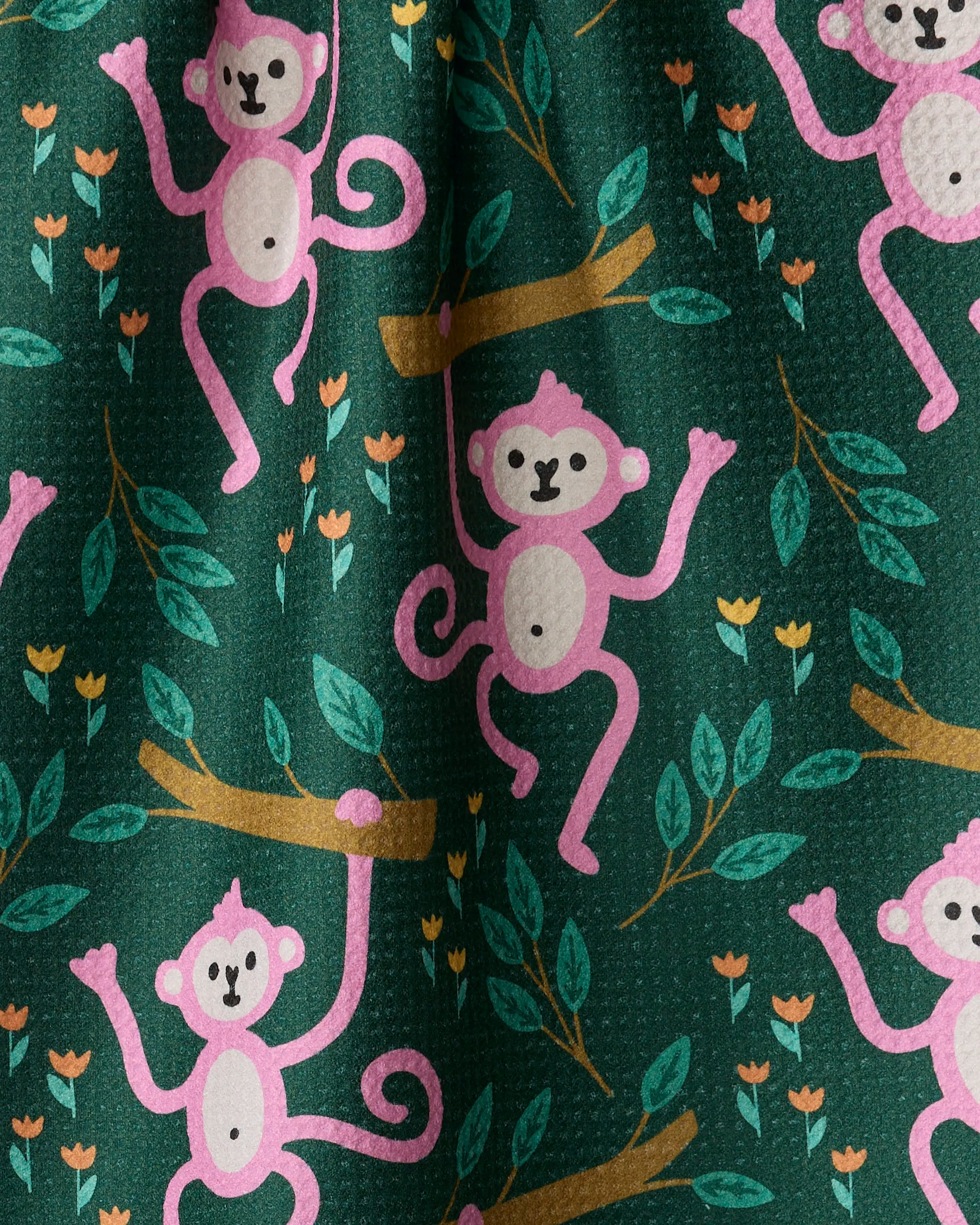Genna Blackburn's "Monkeys" kitchen towel features pink cartoon monkeys swinging among green leaves and orange flowers on a dark green background, all made from recycled materials.