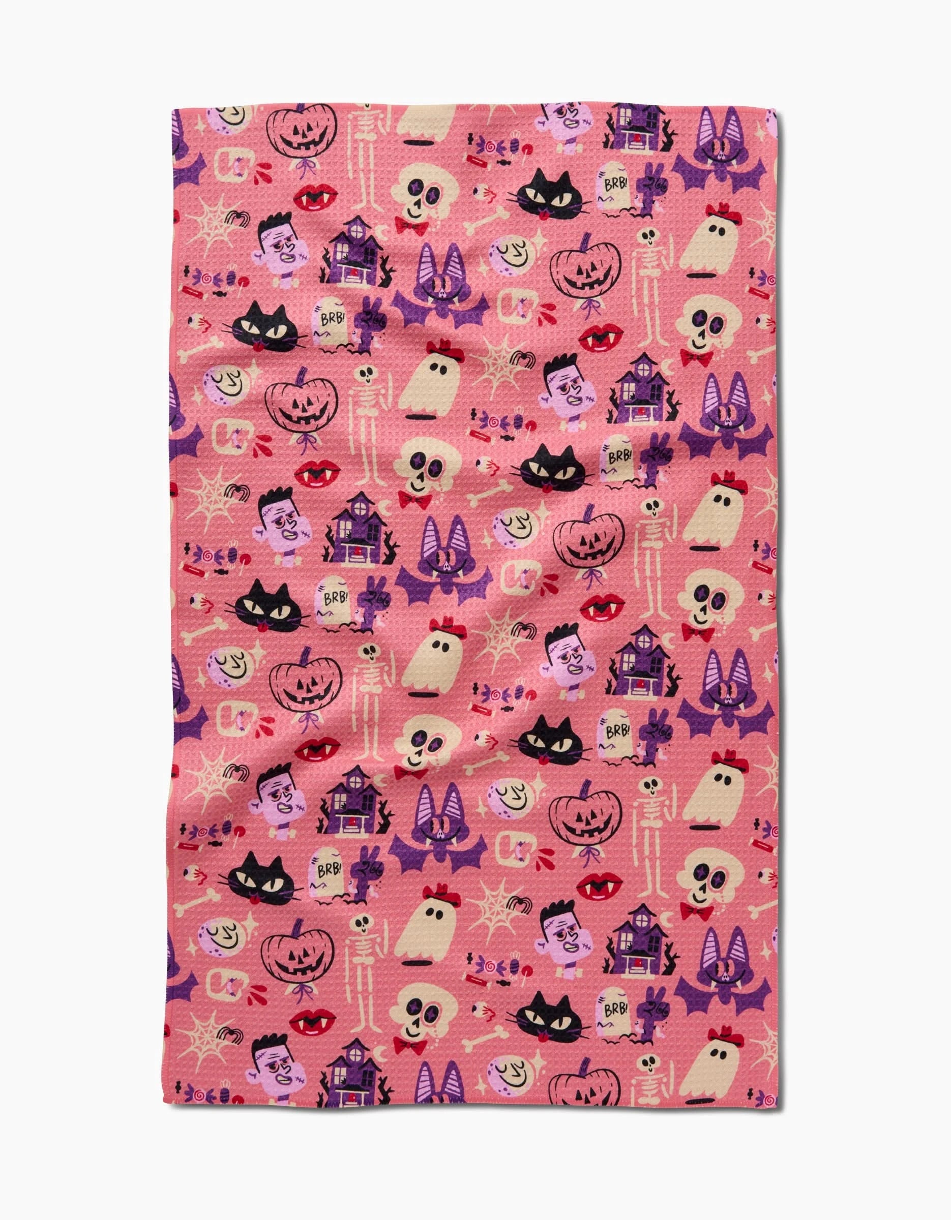 The Carly Berry Monstermash is a pink kitchen tea towel with a repeating Halloween pattern—ghosts, jack-o’-lanterns, bats, skulls, and more in purple, black, orange & white—made from ultra-absorbent recycled materials.