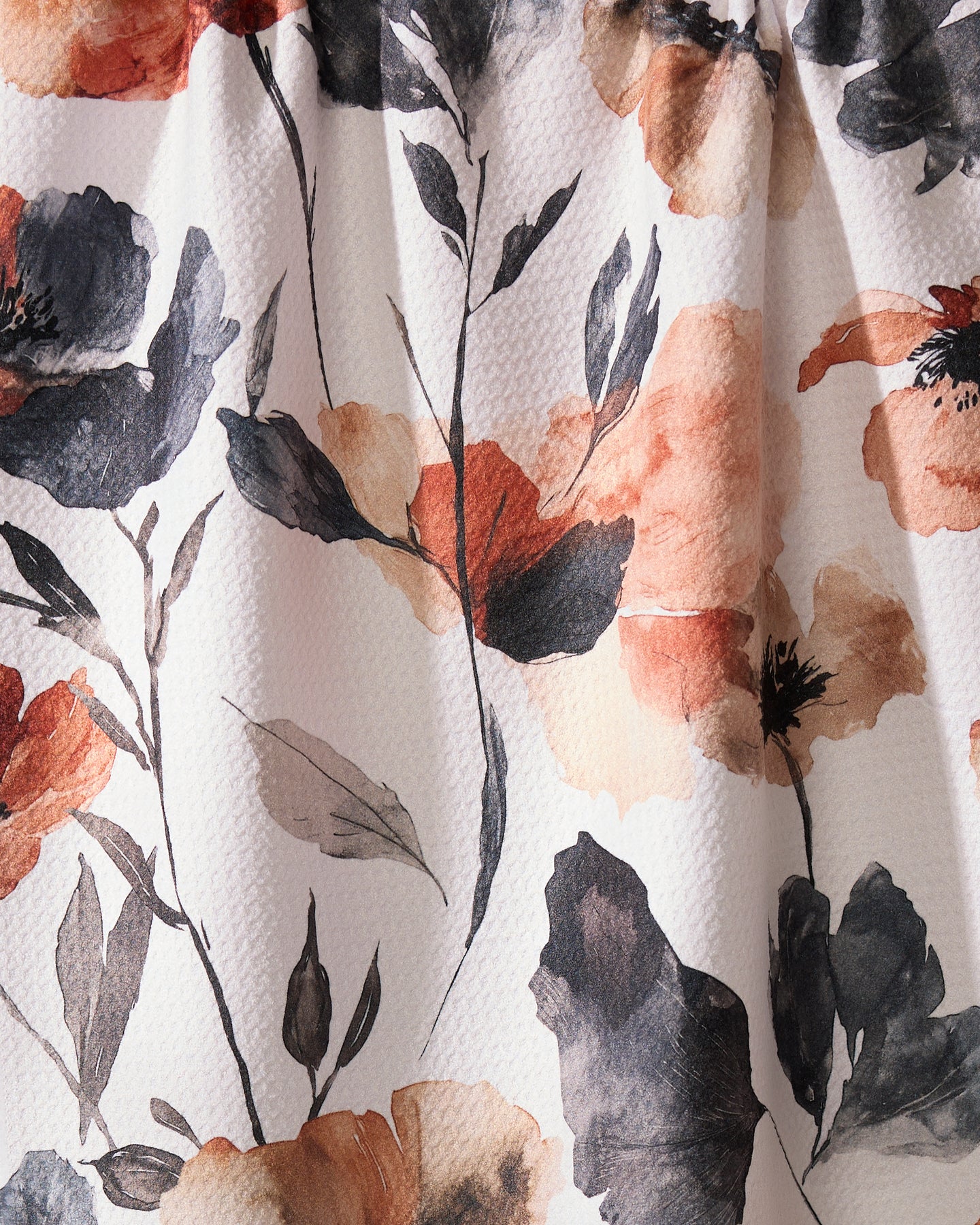 A close-up of the Geometry Moody Poppy kitchen towel, showcasing its textured surface and floral watercolor print in black, orange, and beige on a white background.
