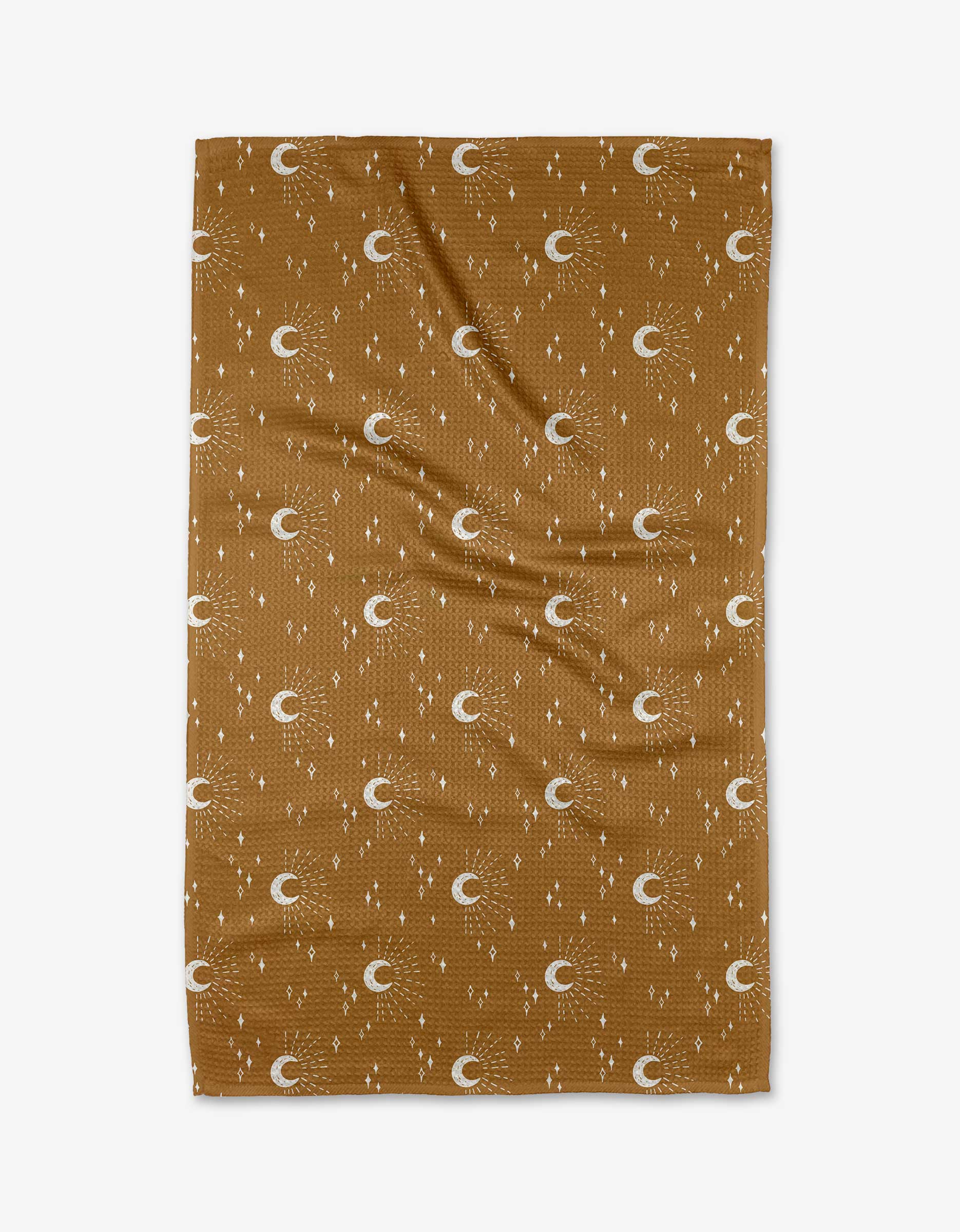 The Moon Craft tea towel by Hufton Studio features a brown textured fabric with a white crescent moon, star, and dot pattern. The quick-drying towel is shown laid flat with slight wrinkles visible.