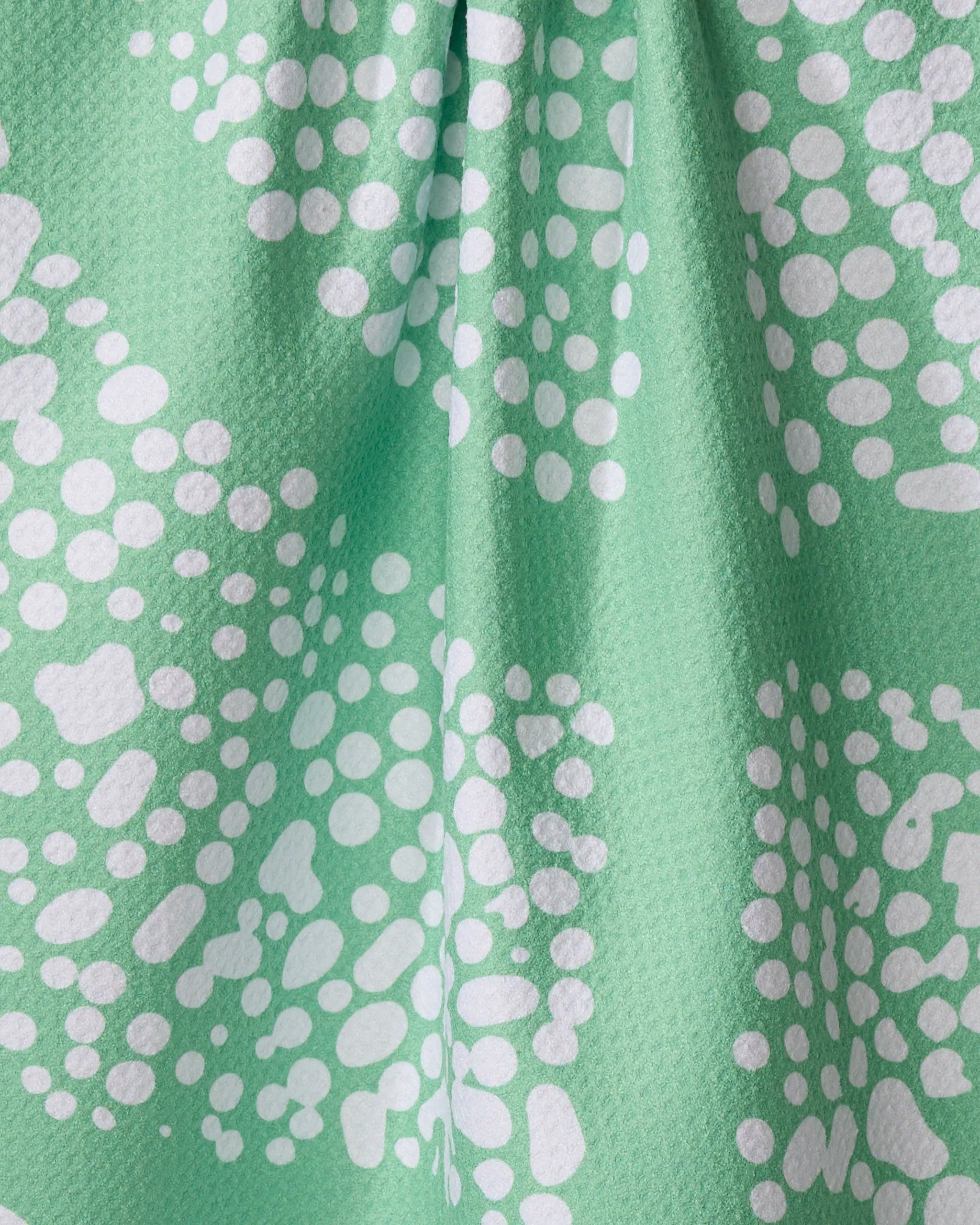 Close-up of the Sissy Moon "Moon Rock" dish towel in green, featuring quick-drying fabric with a textured surface and white abstract dot clusters. Gentle folds create shadows, highlighting its modern design.