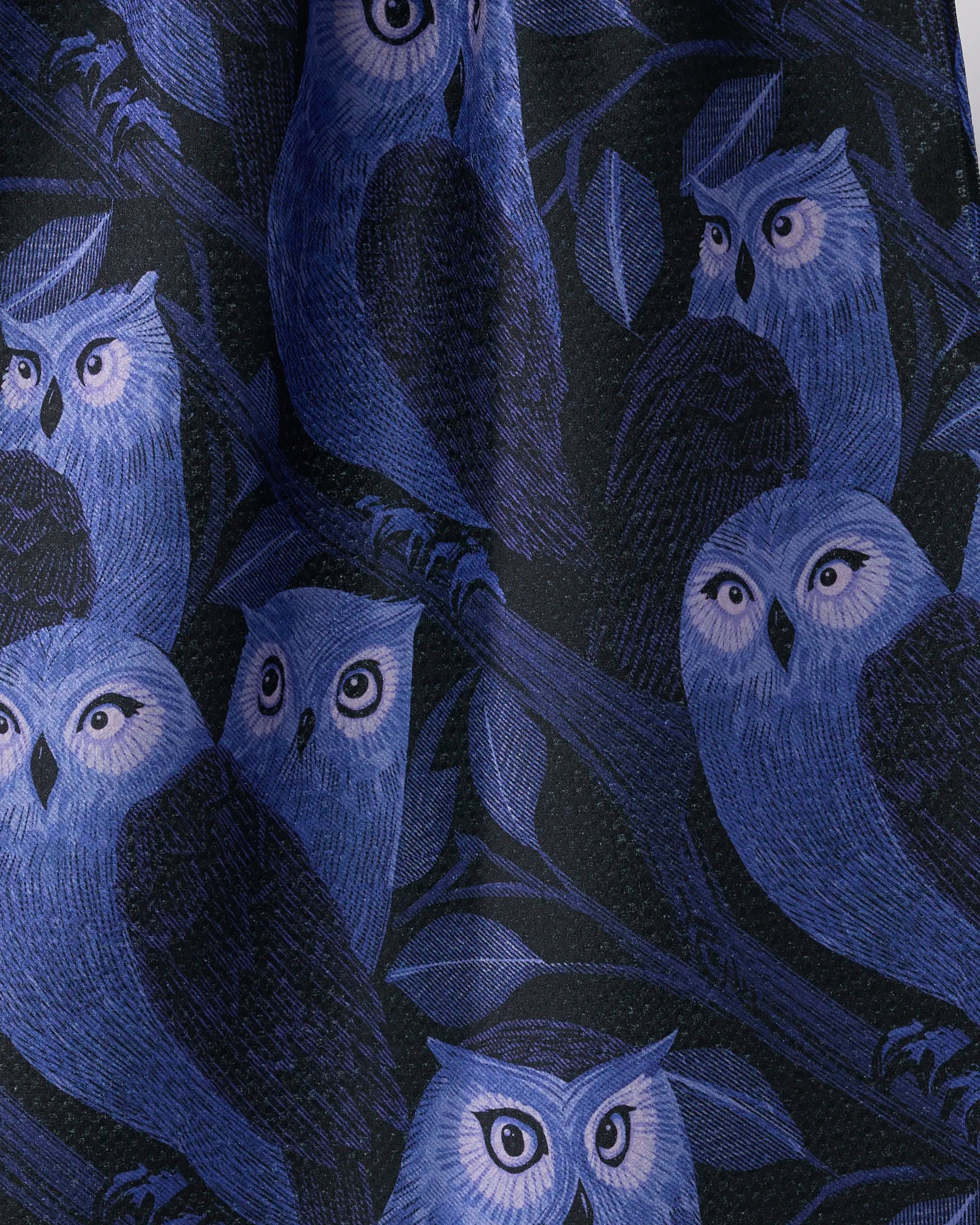Moonfeather by Geometry features expressive blue and purple owls perched on branches with leaves, set against a dark background—perfect for an eco-friendly kitchen or tea towel made from recycled materials.