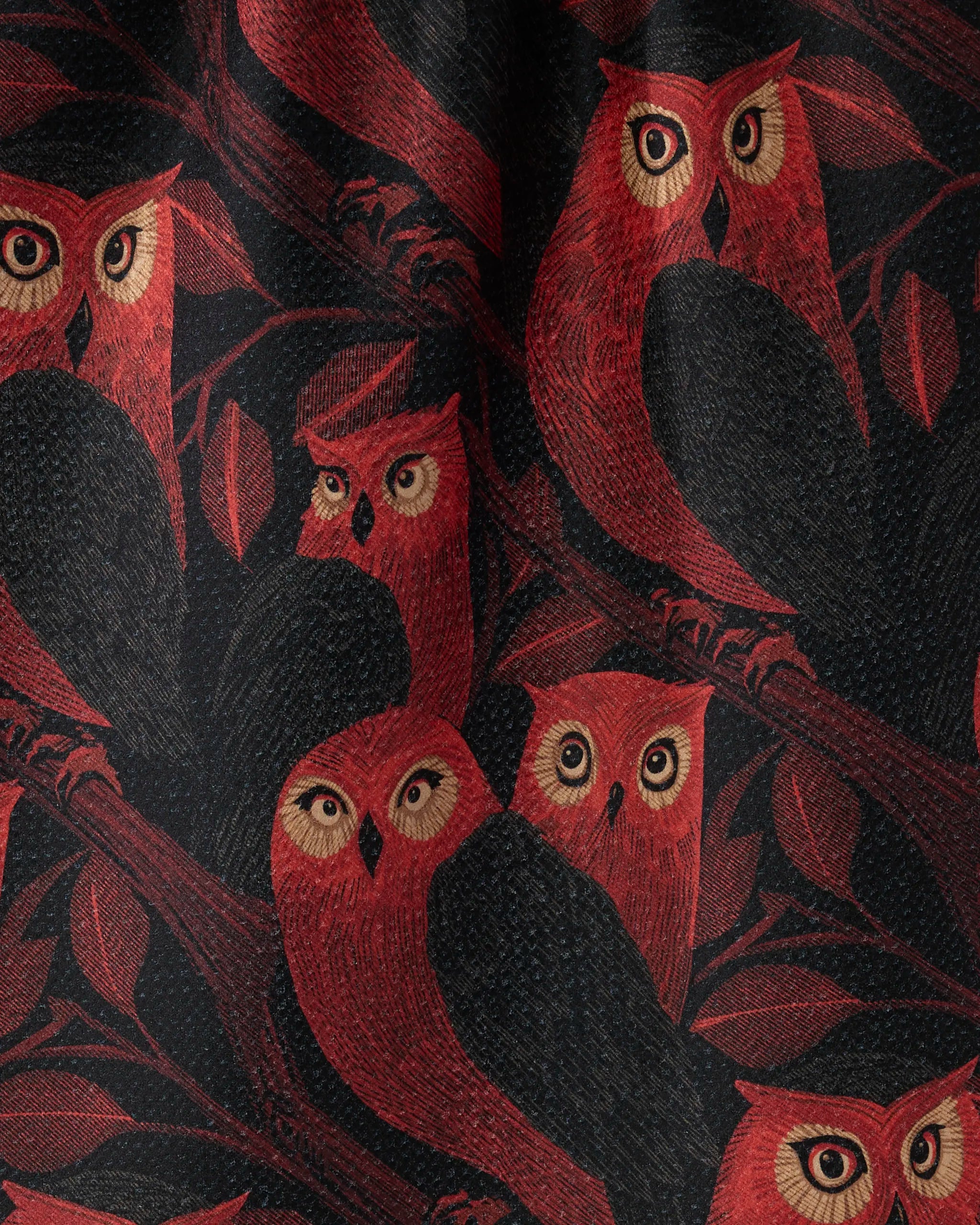 The Geometry Moonfeather tea towel features a dark background with stylized red and orange owls with large eyes perched on leafy branches.