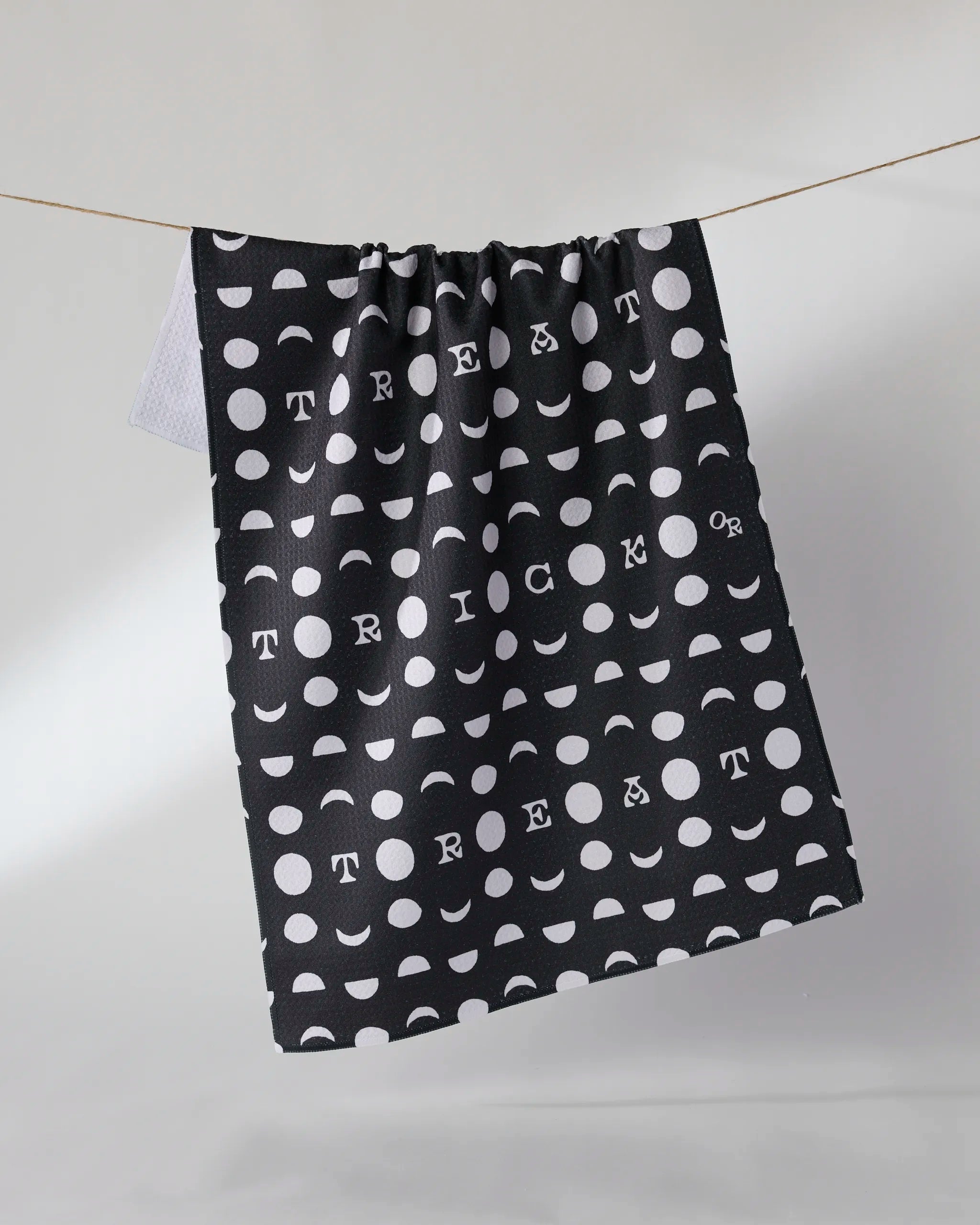 The Geometry Moonlit Mischief tea towel is ultra-absorbent and features a black design with white geometric dots, semicircles, and spaced-out "TRICK OR TREAT" lettering—perfect for festive kitchen decor.