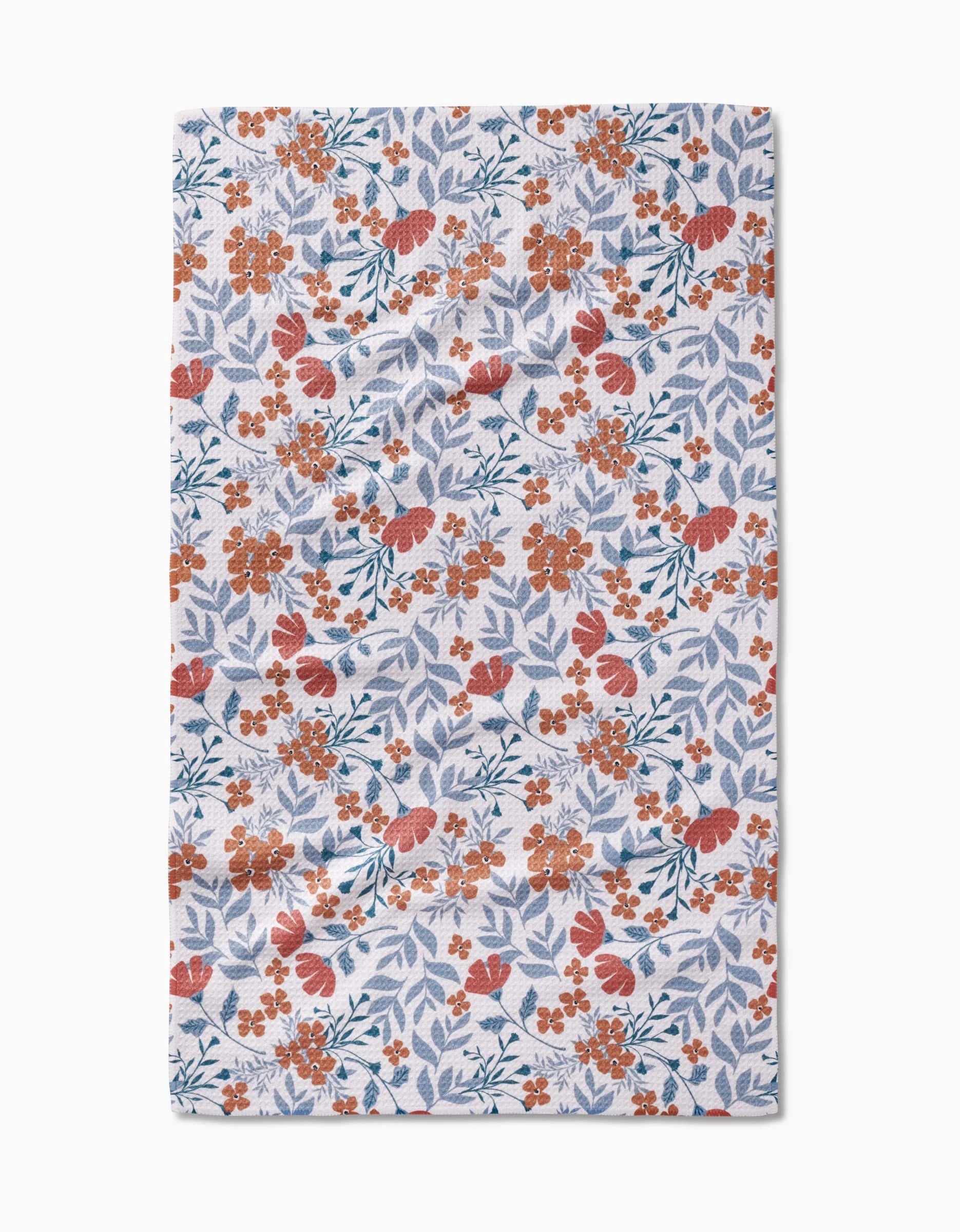 The Morning Blooms tea towel by Charlie Rowan Designs features orange-red flowers and light blue leaves on white, with a dense floral pattern spread evenly across recycled material.