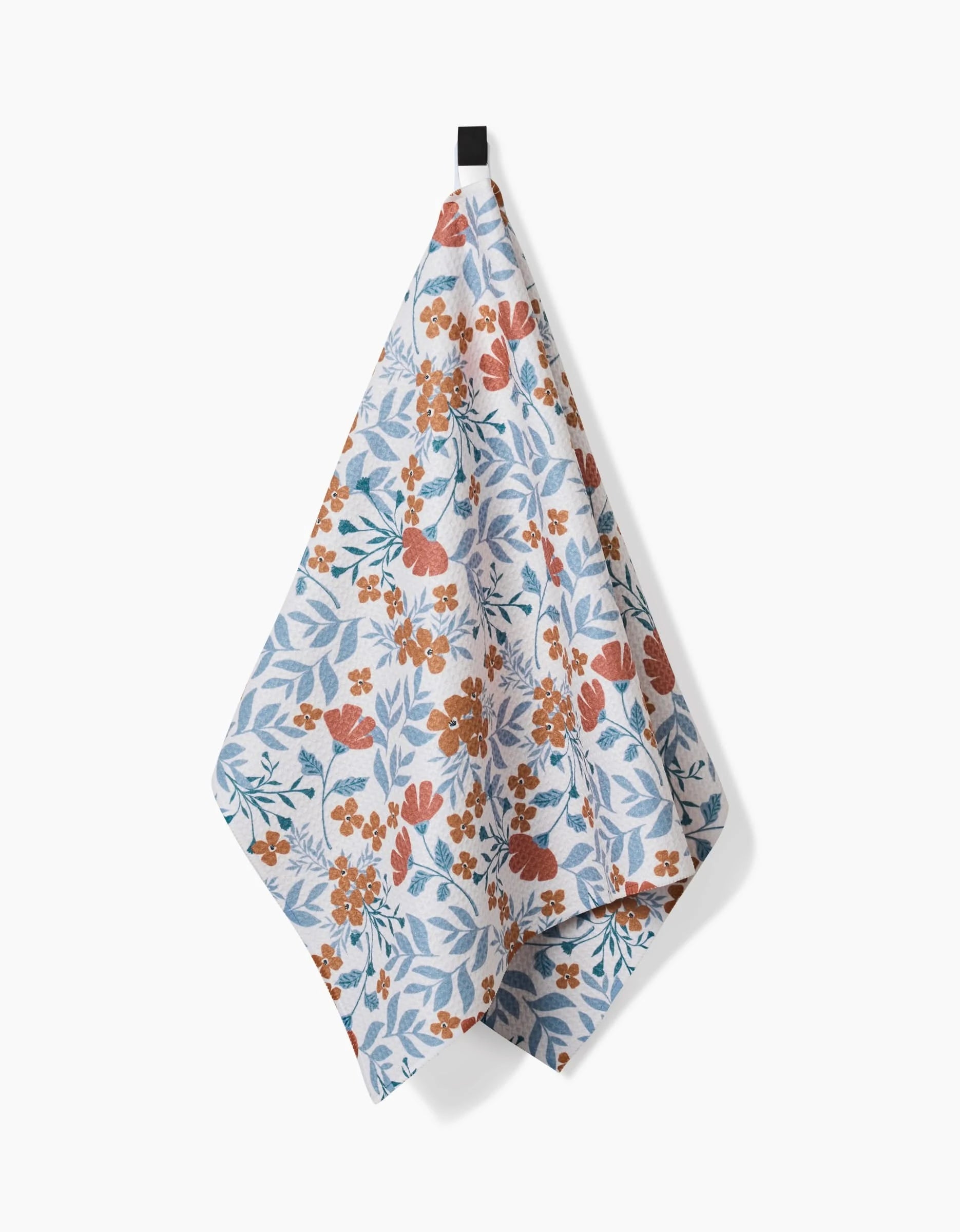 The Morning Blooms tea towel by Charlie Rowan Designs features an orange and blue floral pattern on Geoweave fabric, hanging from a black loop against a plain white background.