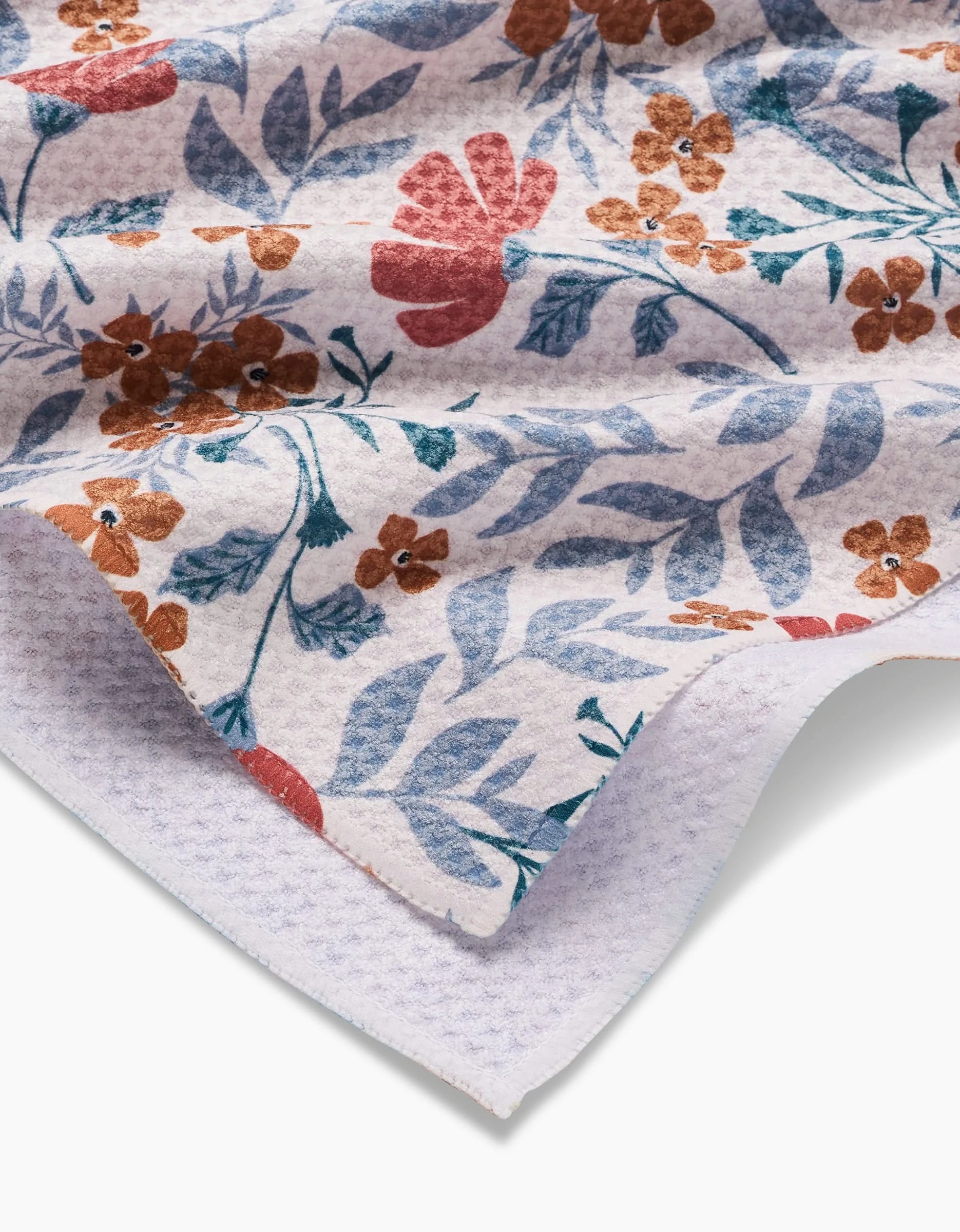 A close-up of Charlie Rowan Designs’ Morning Blooms Tea Towel shows its textured Geoweave fabric, with red, orange, and blue floral patterns on white. The softly folded towel highlights its unique weave and vibrant design.