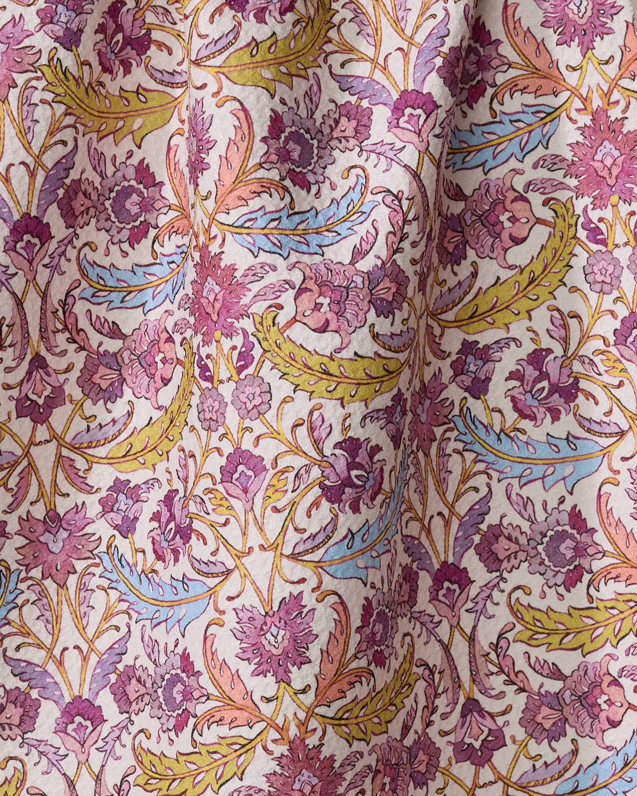 The Morning Glory tea towel by Maayan Alper-Swan features a vintage-style floral pattern in pink, purple, yellow, blue, and orange. Made from recycled materials, it drapes gracefully to showcase its intricate design.