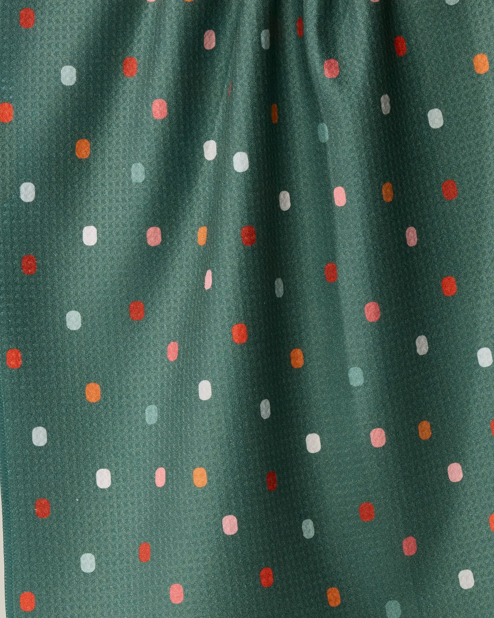 Introducing Moss Tile Shuffle by Geometry: This dark green fabric features small, evenly spaced dots in white, red, pink, and orange. Subtle gathered folds create gentle shadows and texture—making it an ideal choice for a charming kitchen towel crafted from recycled materials.