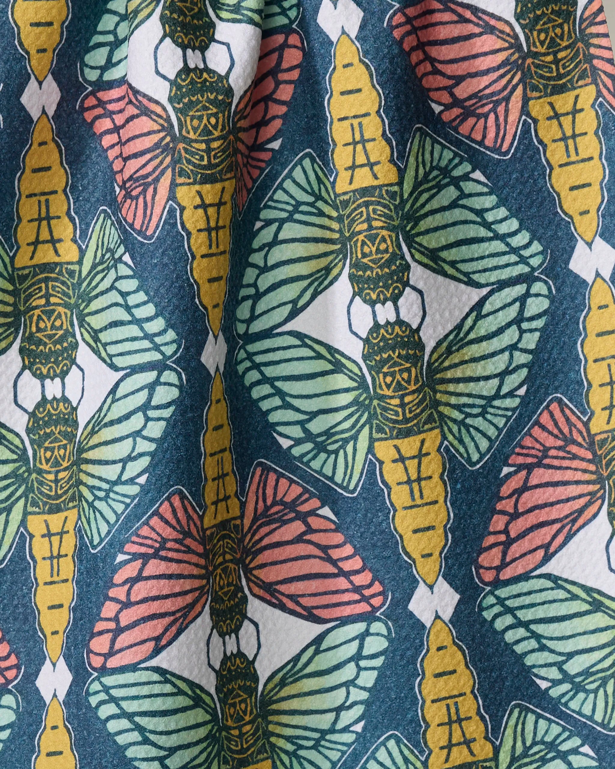 The "Moths" tea towel by Renee Fly features repeating yellow-bodied moths with green or red wings on a dark teal background with white diamonds. Made from quick-drying, recycled materials.
