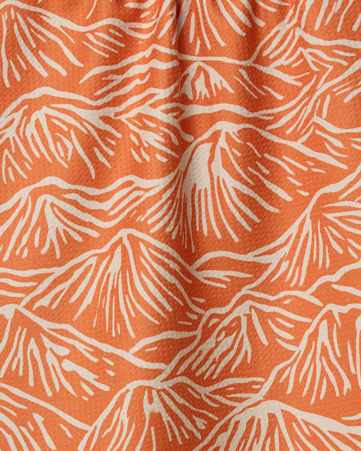 The Mountain Range towel by Geometry features an orange fabric with a white abstract mountain pattern. Its wavy, organic lines resemble peaks and ridges, and the ultra-absorbent texture includes subtle folds for added dimension.