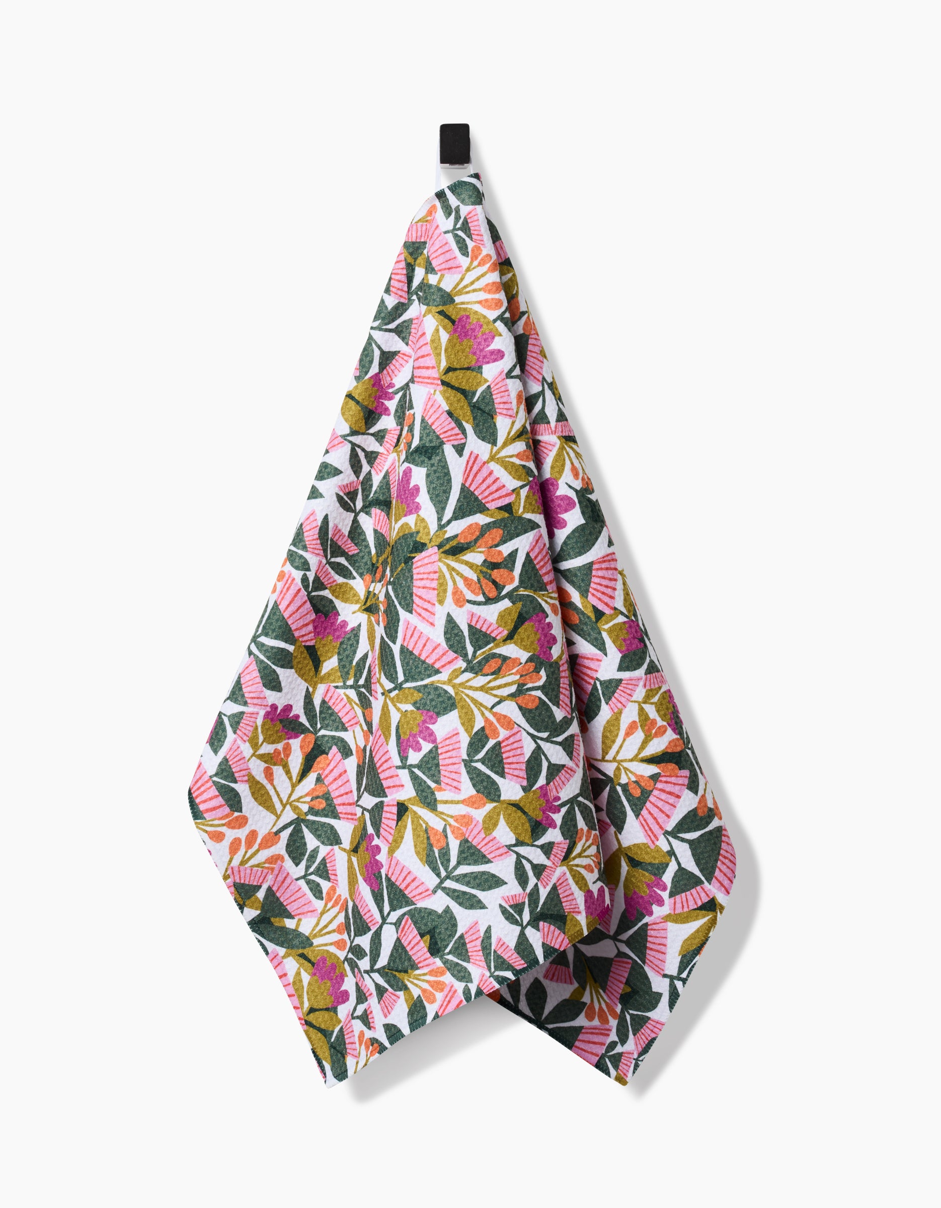 The Moxie Mauve tea towel by Lisa Nelson is made from recycled materials and features a vibrant botanical design with green leaves and pink, orange, and yellow flowers. It hangs from a black loop against a white background.