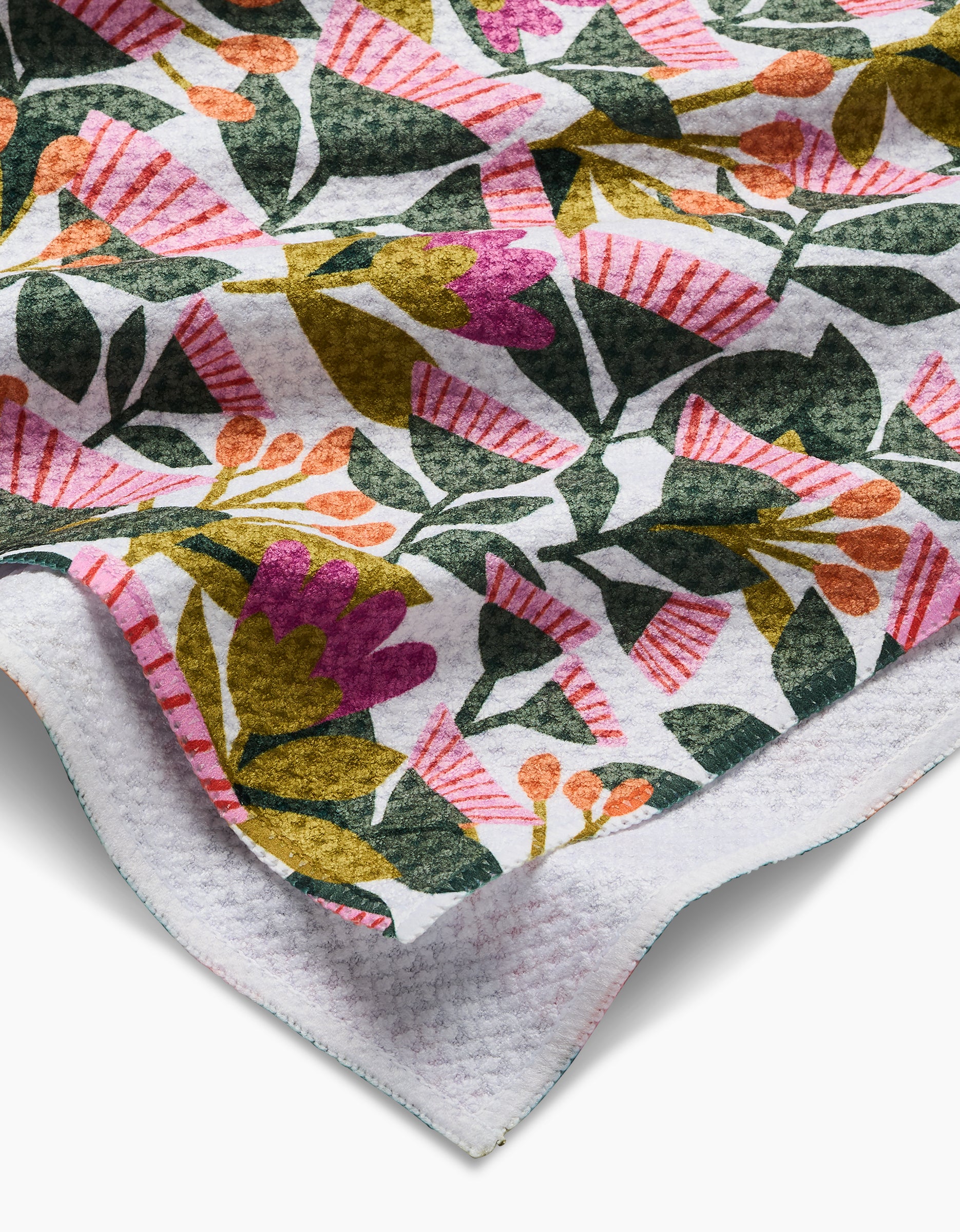 A close-up of the Lisa Nelson Moxie Mauve tea towel, showcasing pink, orange, and purple flowers with green leaves on white Geoweave fabric for a soft, textured look.