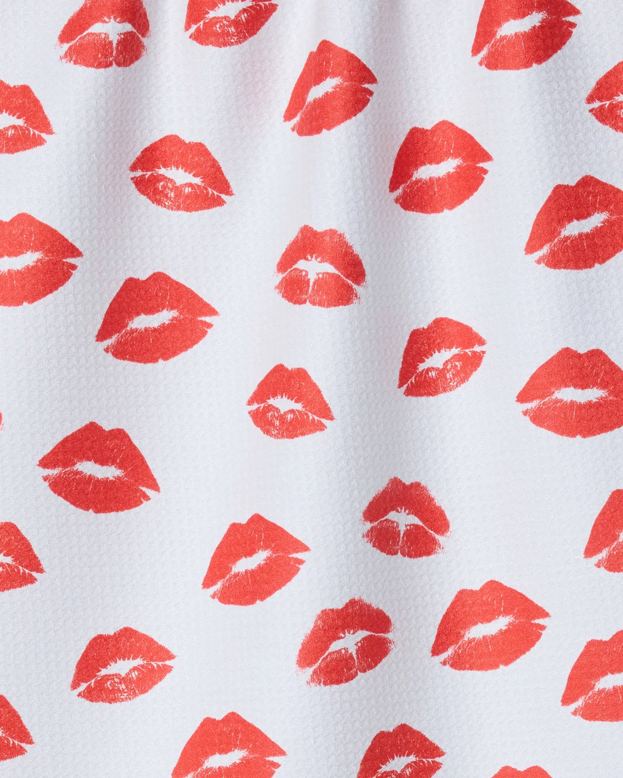 The Geometry "Muchos Besos" kitchen towel features a repeating pattern of red lipstick kiss prints scattered across white textured recycled fabric.