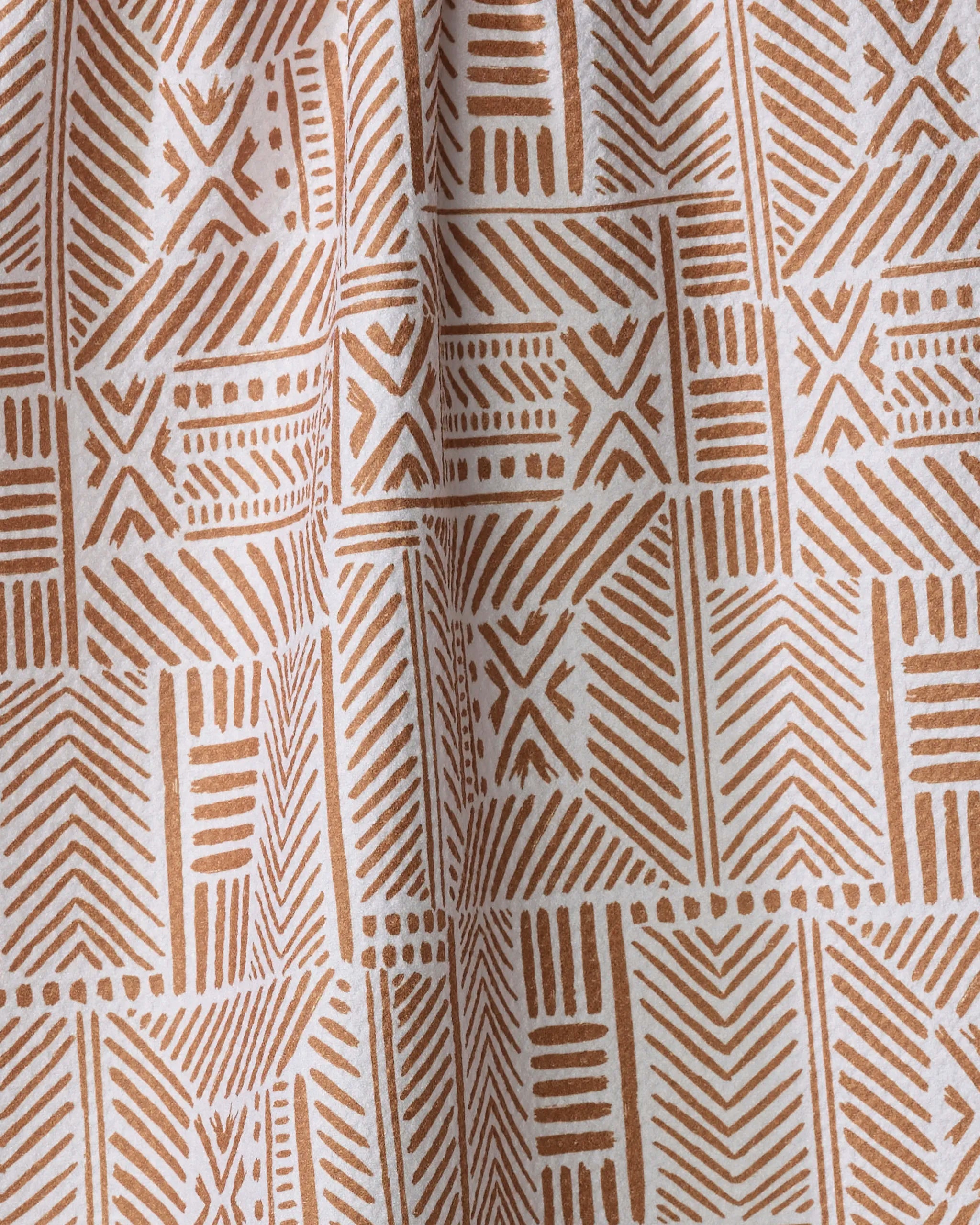 A close-up of Hufton Studio's Mud Cloth Natural recycled kitchen towel shows a brown and white geometric pattern—lines, arrows, and X shapes in a grid—for a textured, tribal-inspired look. The fabric appears slightly gathered.