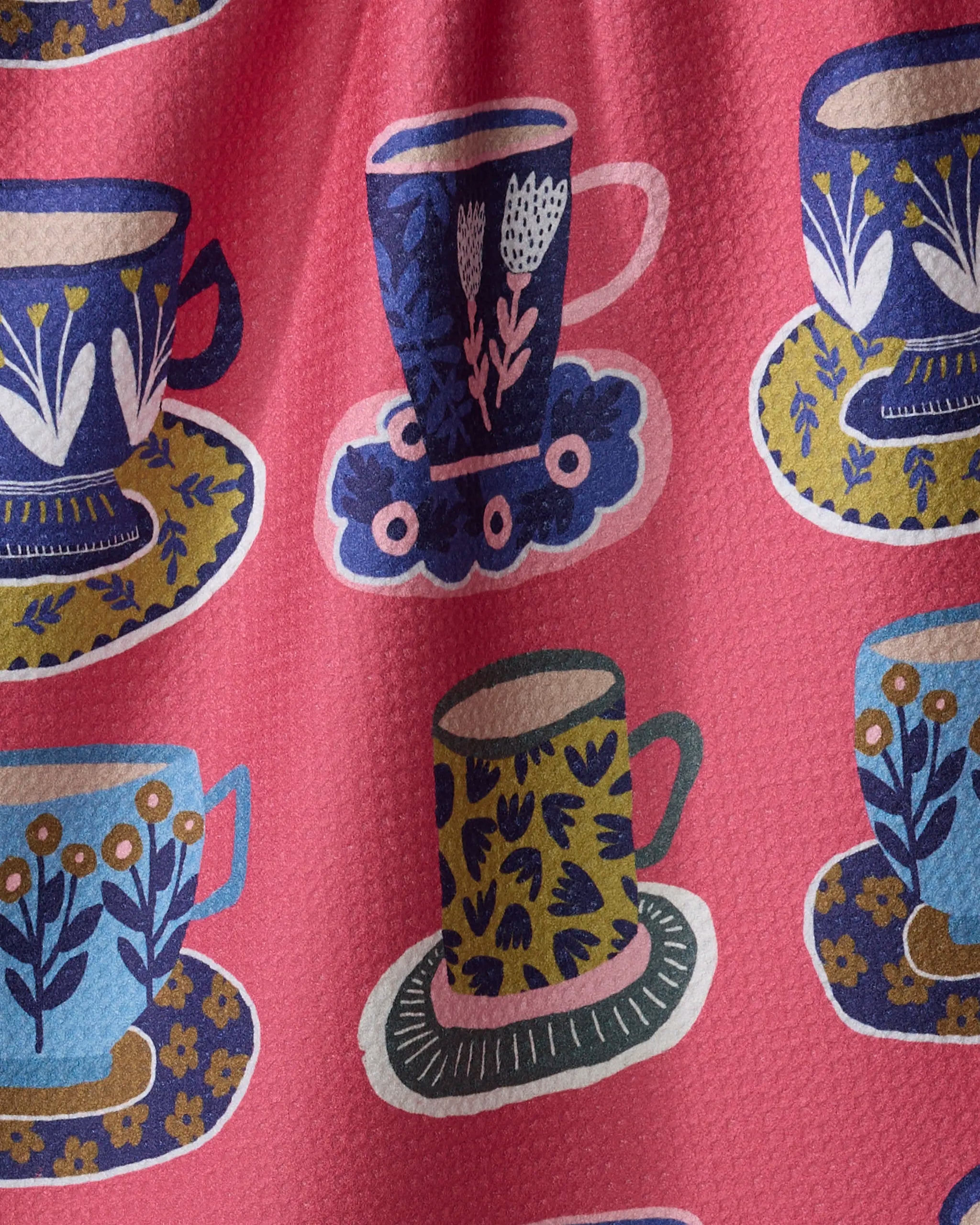 The Mug Set by Cottonflower Studio features a pink textured fabric made from recycled materials, with a repeating pattern of blue, yellow, and green teacups and saucers adorned with floral designs.