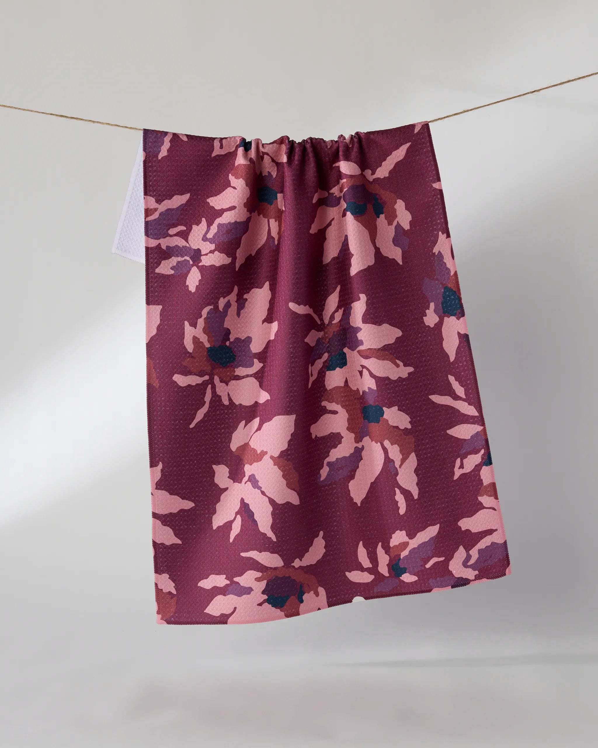 The Geometry Mulberry Bloom kitchen tea towel, made from recycled materials and featuring a pink and blue floral pattern, hangs against a plain light background.
