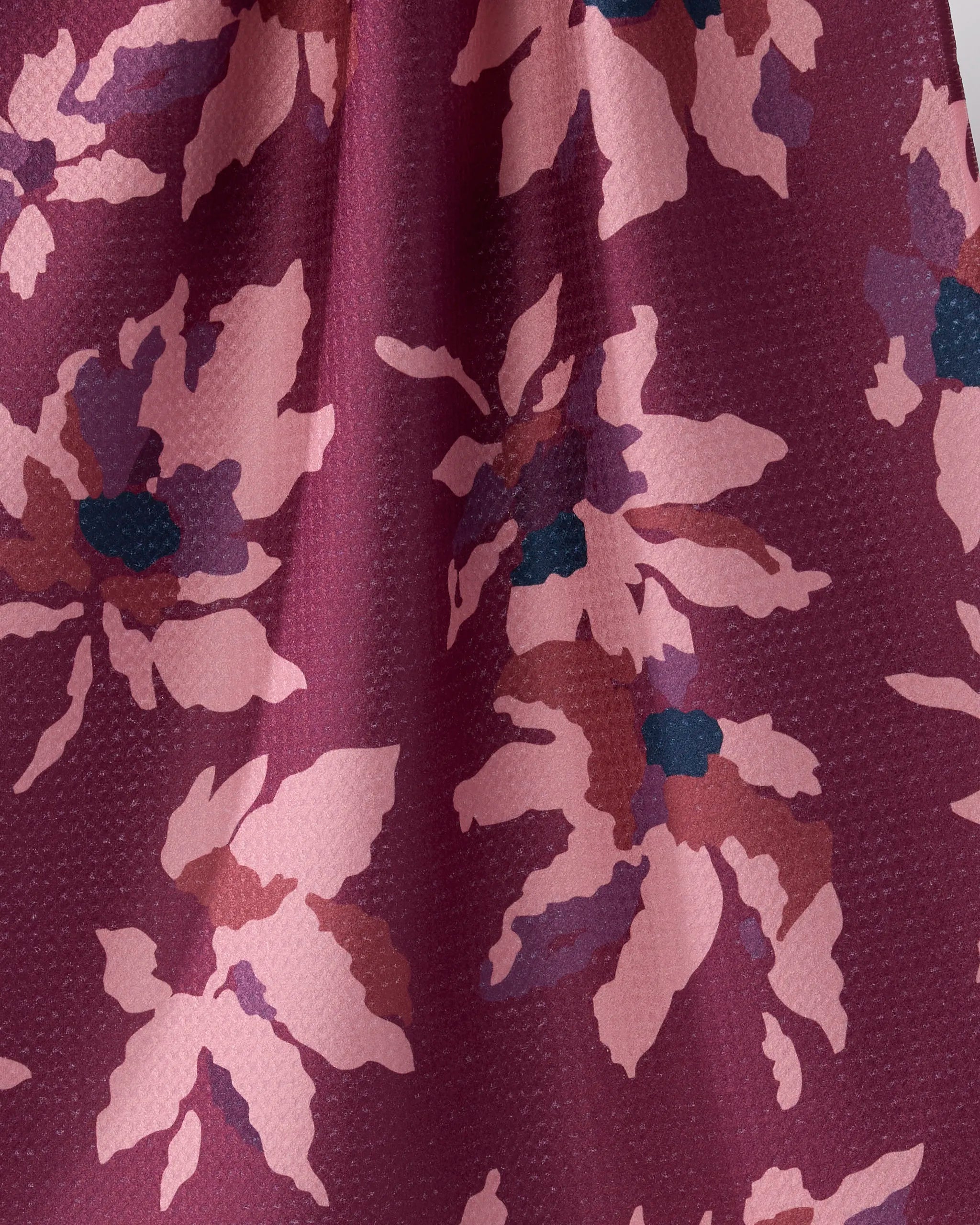 Close-up of the Geometry Mulberry Bloom towel, showing maroon textured fabric with a pink and mauve abstract floral design plus dark blue accents. Made from recycled materials, this ultra-absorbent towel is elegantly draped to highlight its softness.