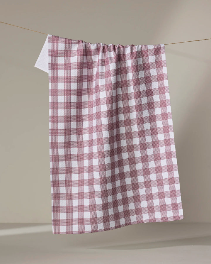 The Buy Guide's Multi Gingham - Wine tea towel hangs on a line against a plain beige background.