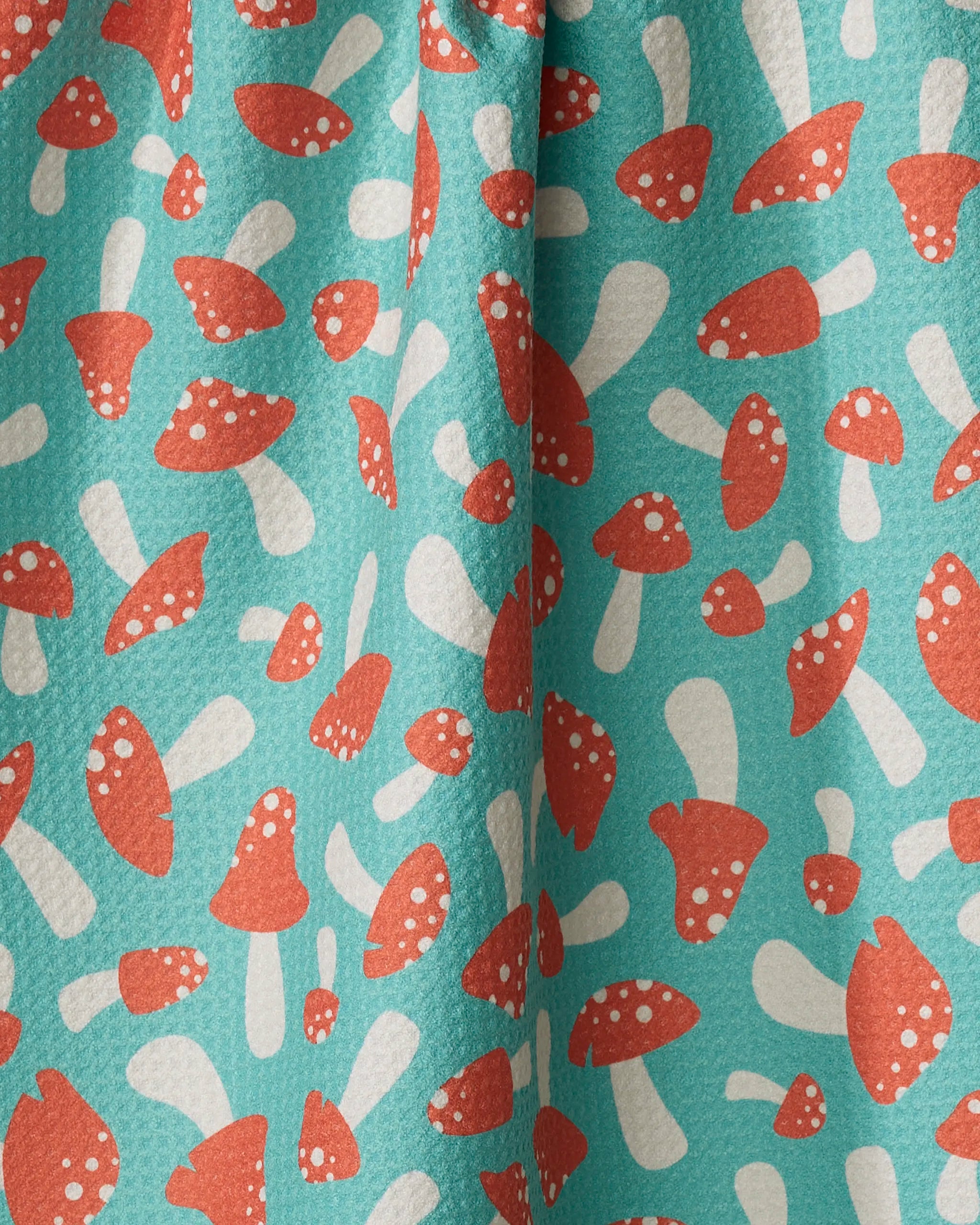 Close-up of the "Mushrooms" kitchen towel by Megan Kampa, featuring a turquoise recycled fabric with playful red and white mushrooms scattered throughout for a vibrant, whimsical design.