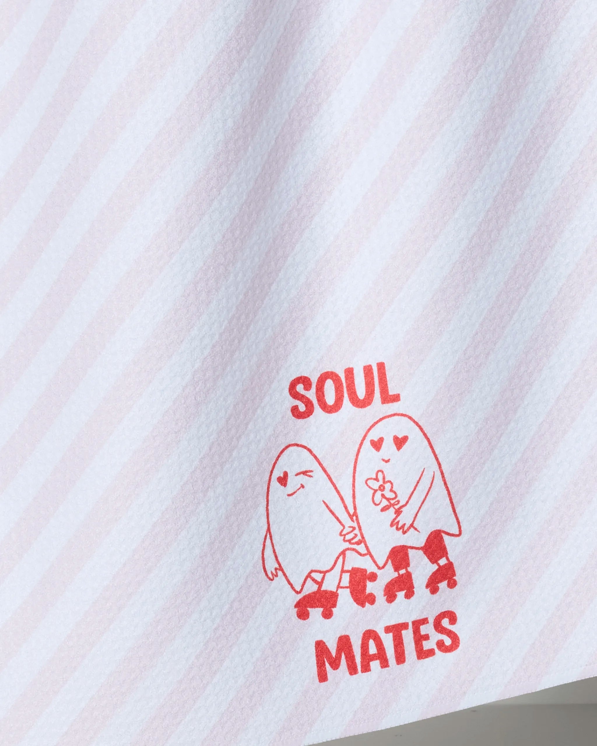 Close-up of Geometry's "My Ghostly Love" tea towel: light pink diagonal stripes, two cartoon ghosts on roller skates holding hands, and SOUL MATES in red uppercase letters above and below the ghosts.
